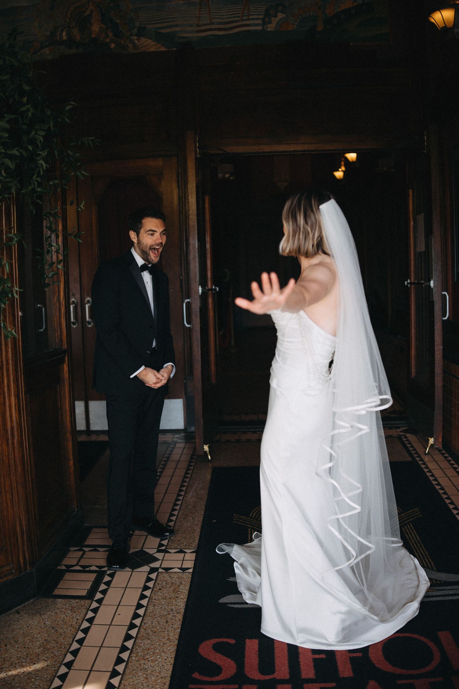Groom reacts with joy as bride reveals her stunning white wedding gown during first look.