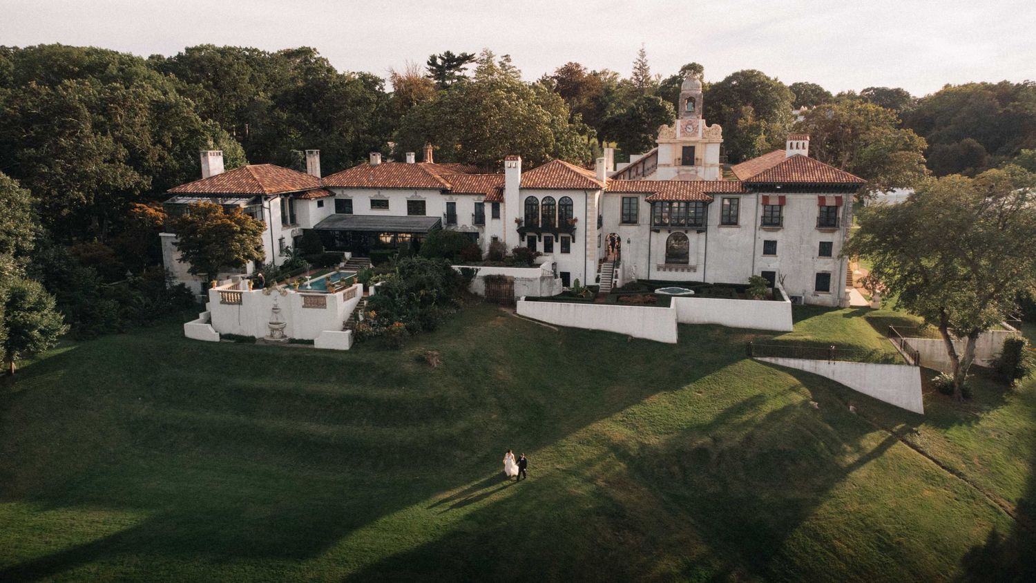 Aerial view of a grand white Mediterranean-style wedding venue estate surrounded by lush greenery.