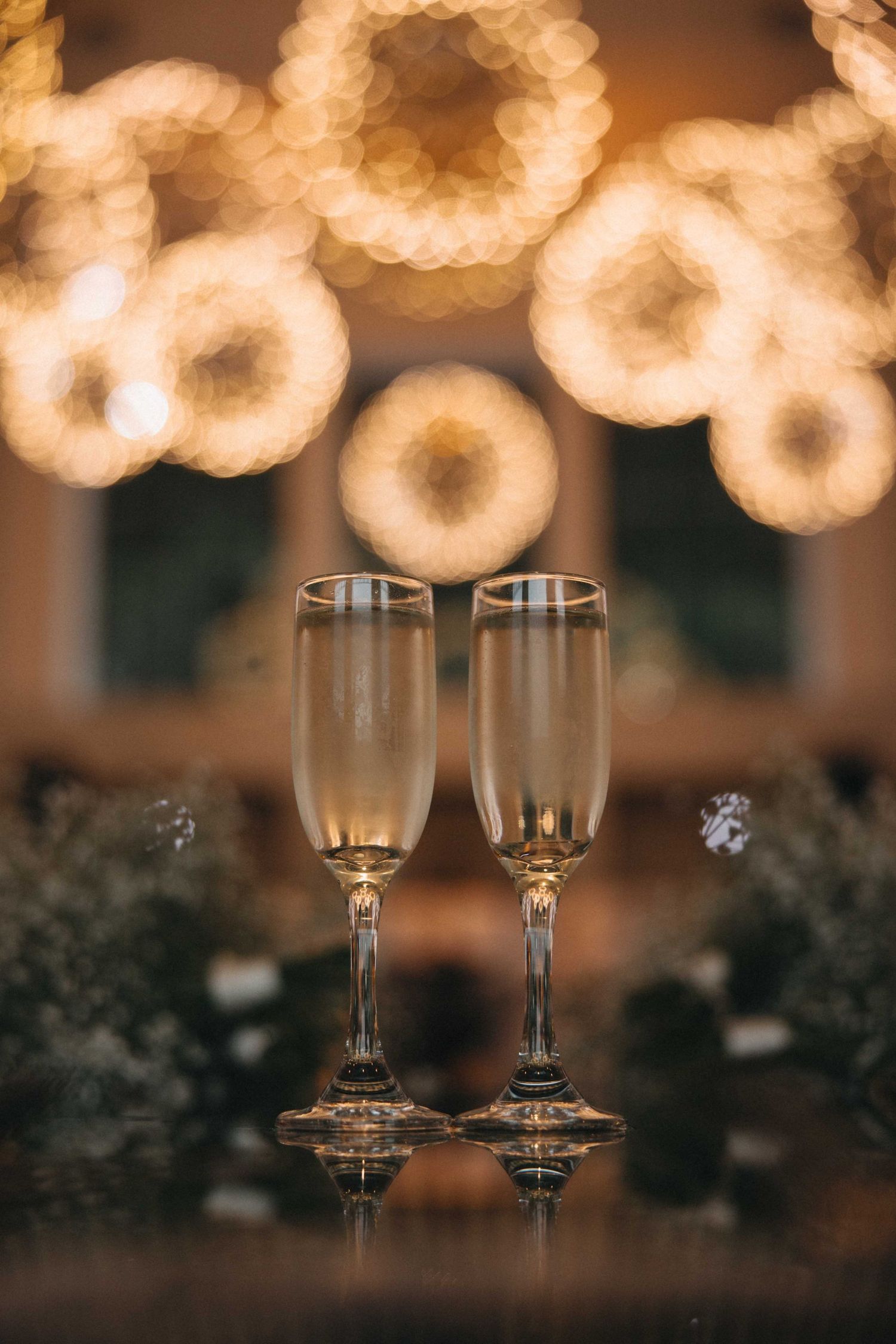 Two champagne flutes on a table with warm bokeh lights glowing in the background.
