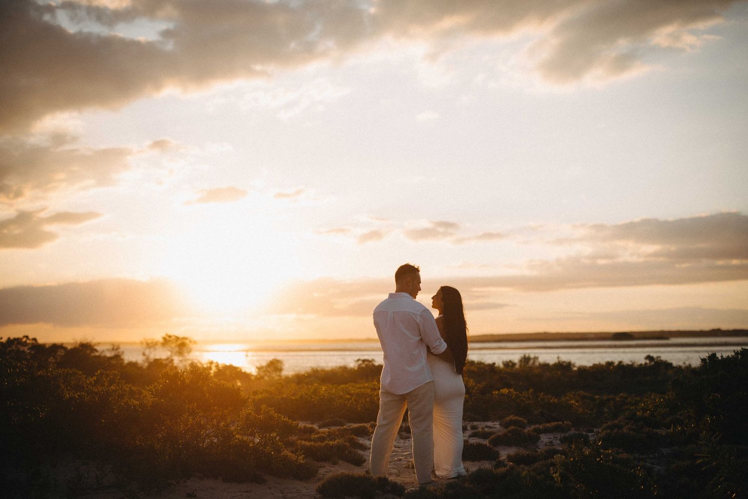 Couple standing together overlooking a serene waterfront landscape at golden sunset.