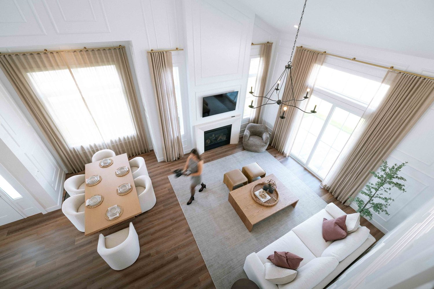 Aerial view of a bright open-plan living and dining room with hardwood floors and large windows.