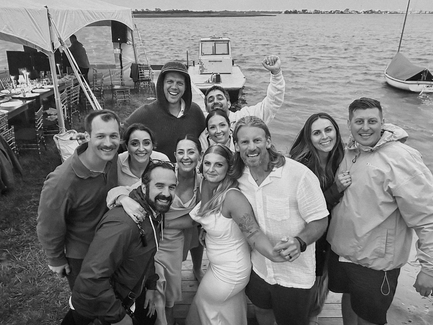 Black and white photo of wedding party group smiling by waterfront dock.