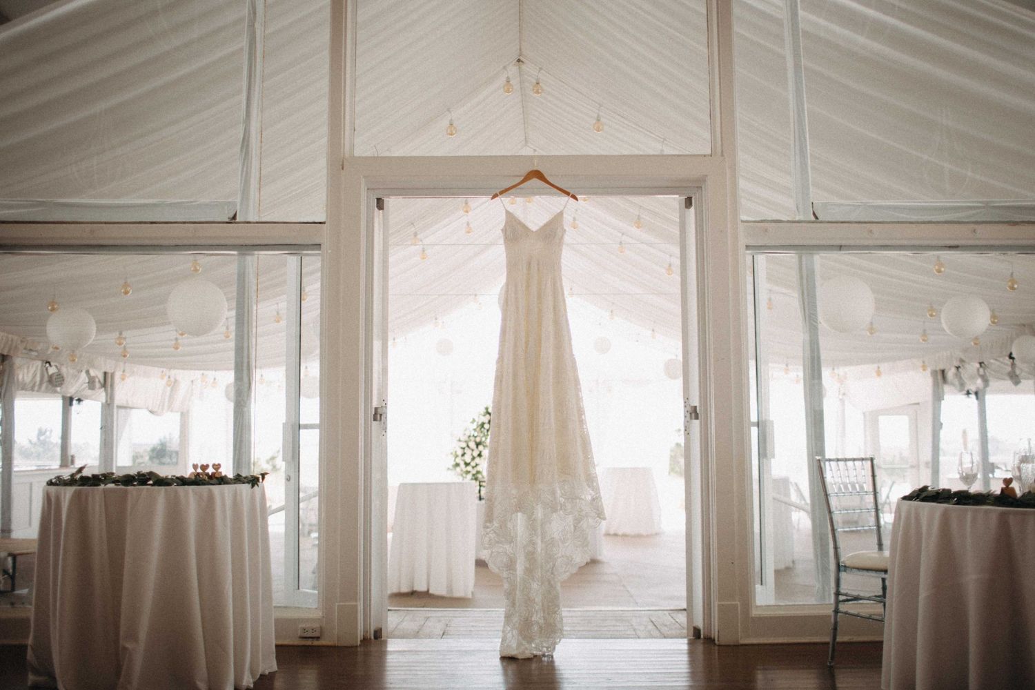 Elegant white lace wedding dress hanging in a bright tent venue before the ceremony.