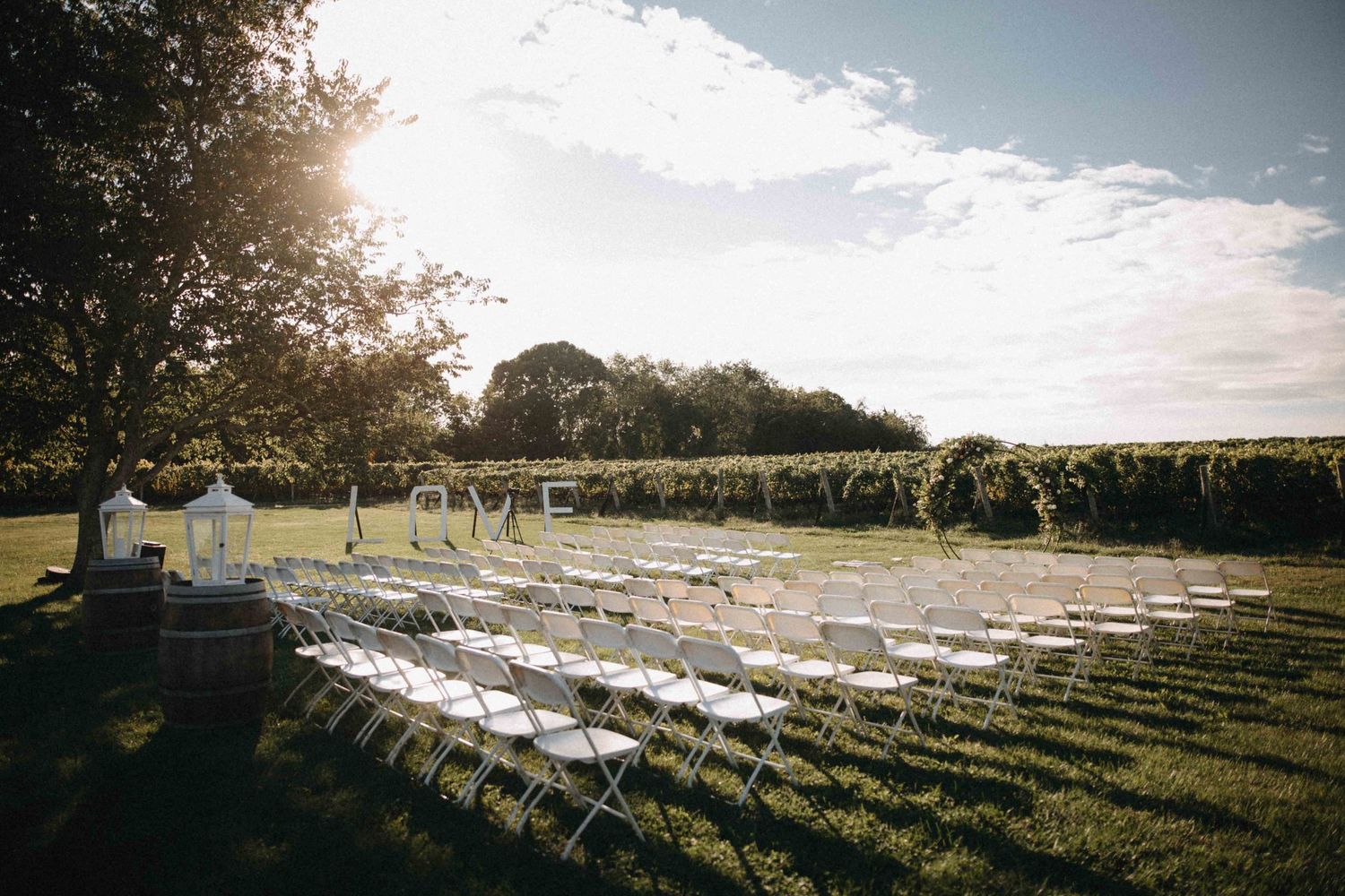 White chairs arranged in rows for outdoor vineyard wedding ceremony under bright sunny sky.