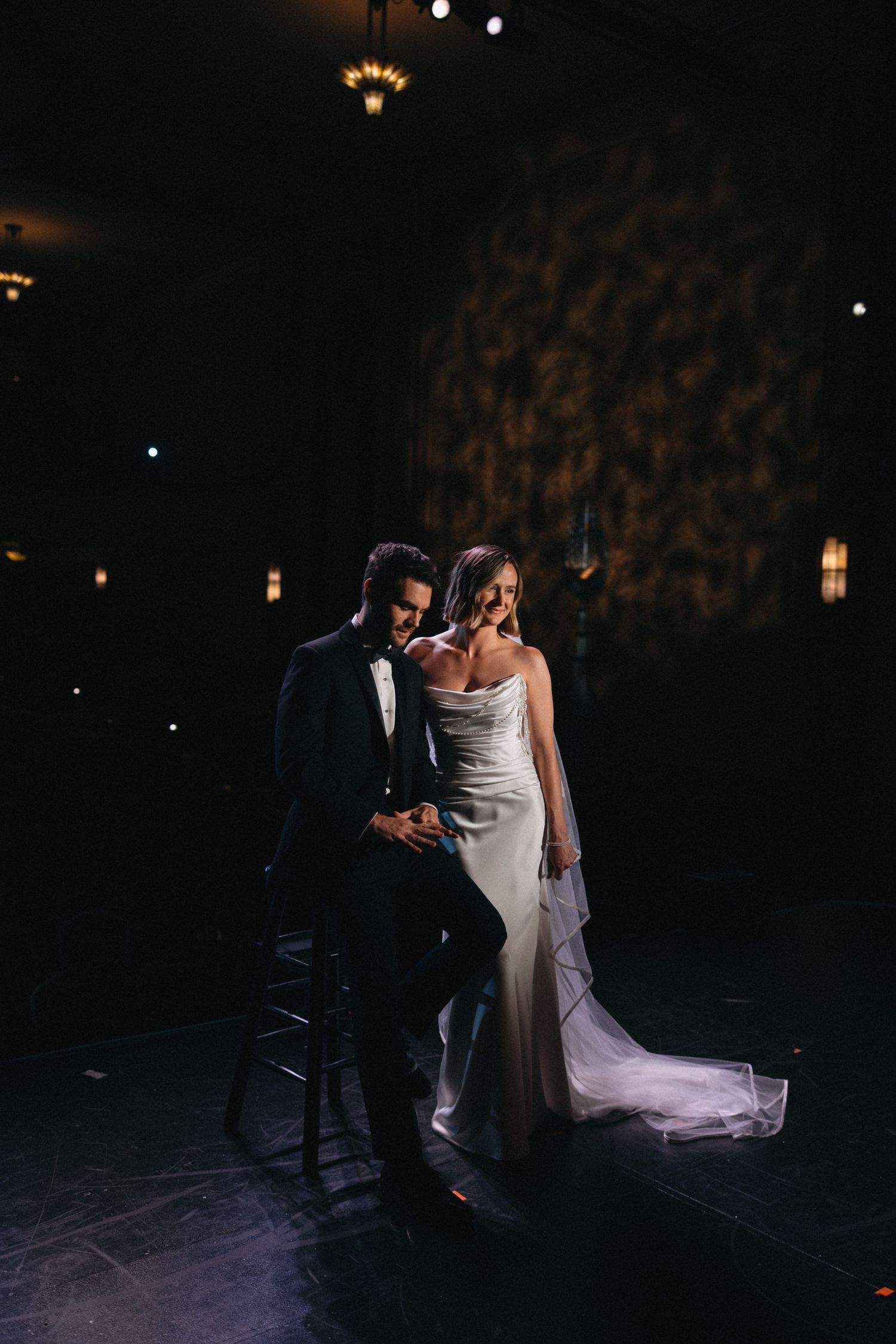 Elegant bride and groom pose in dramatic dark lighting at sophisticated indoor wedding reception venue.
