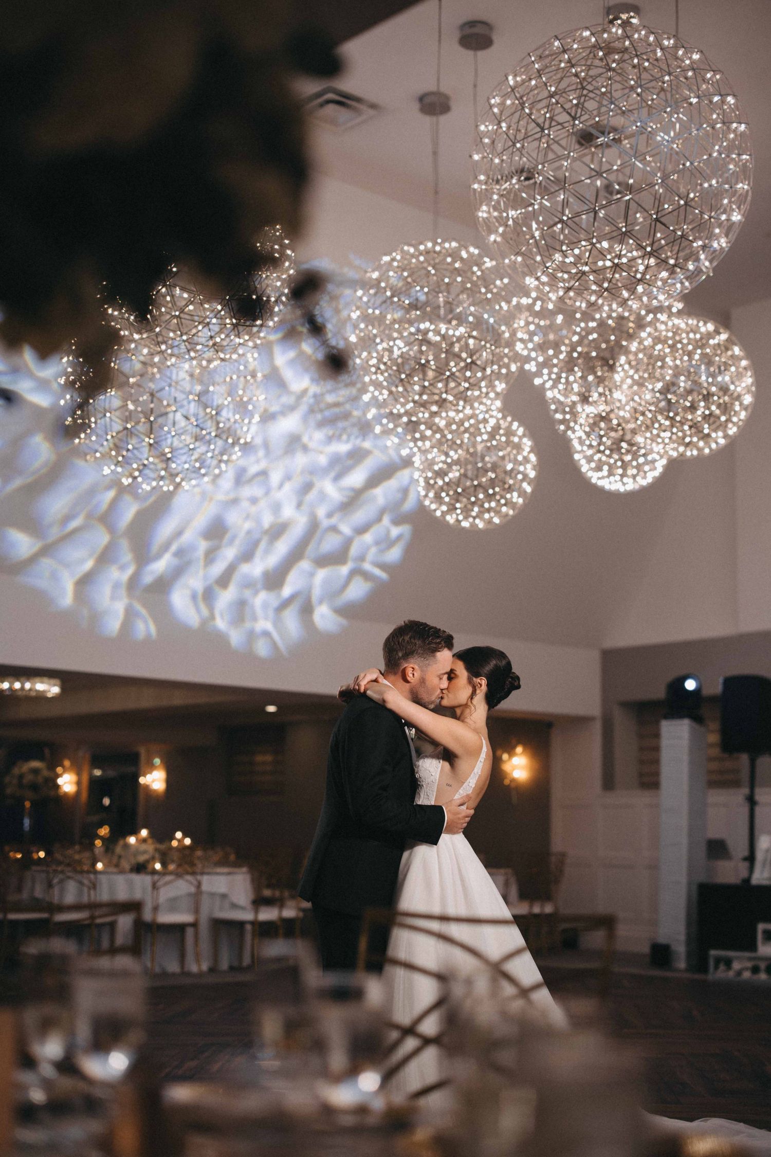 Bride and groom sharing first dance beneath stunning spherical fairy light chandeliers.