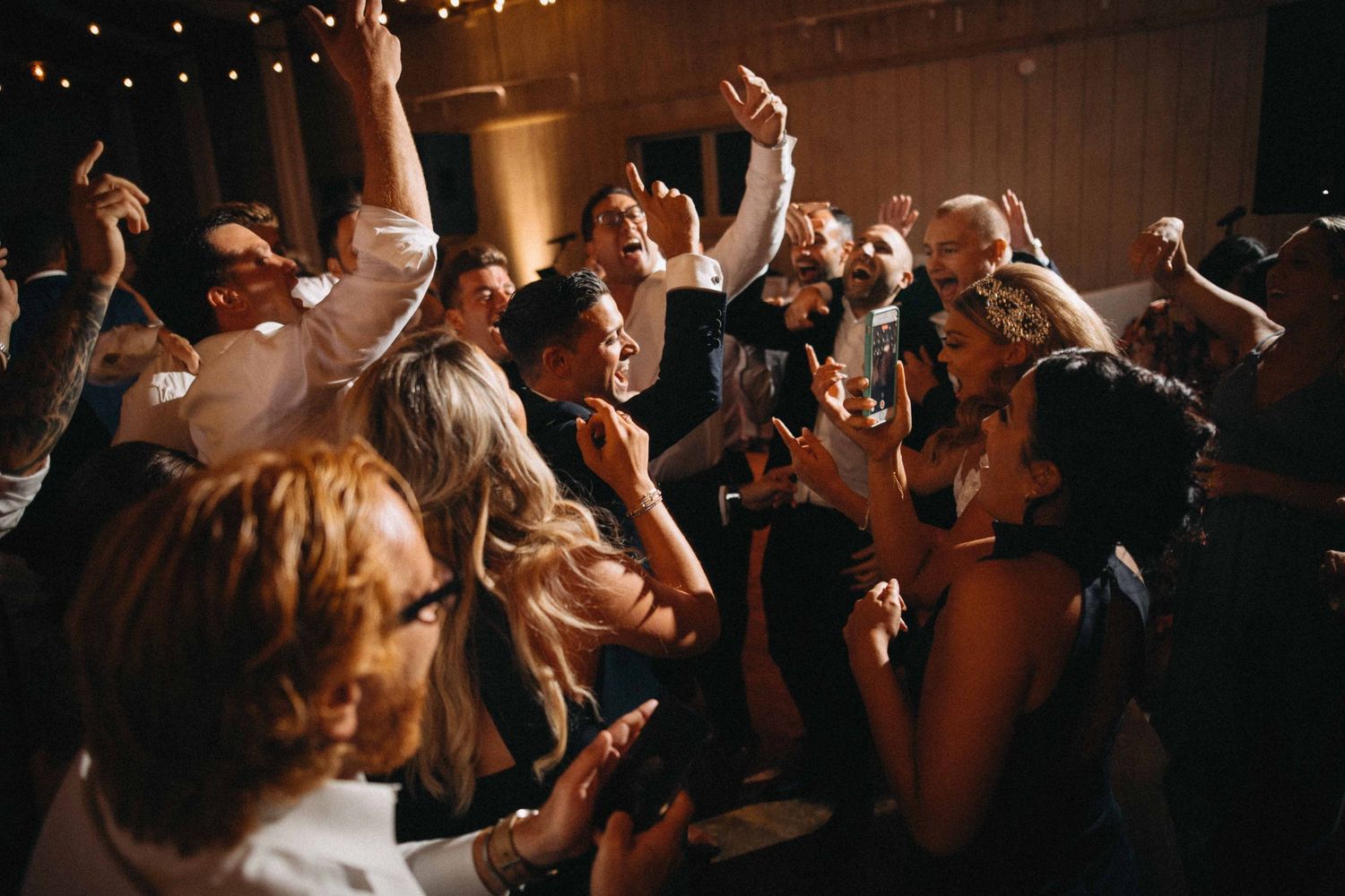 Energetic wedding reception dance floor packed with celebrating guests under warm lights.