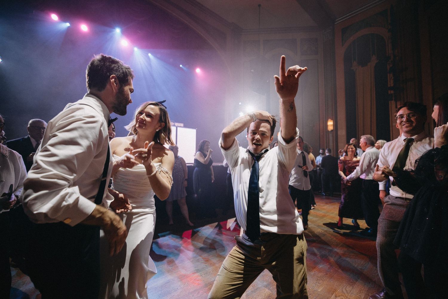 Guests dance energetically on colorful lit dance floor during lively wedding reception celebration.