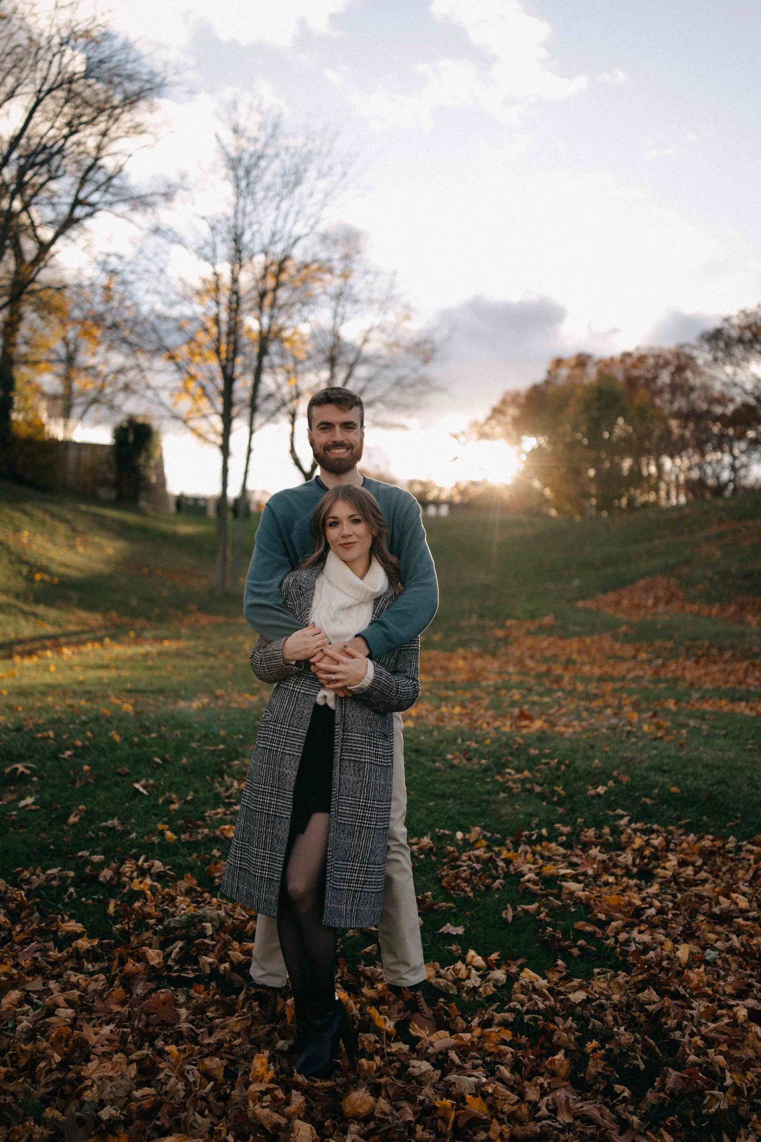 Couple embracing in an autumn park at golden sunset surrounded by fallen leaves.