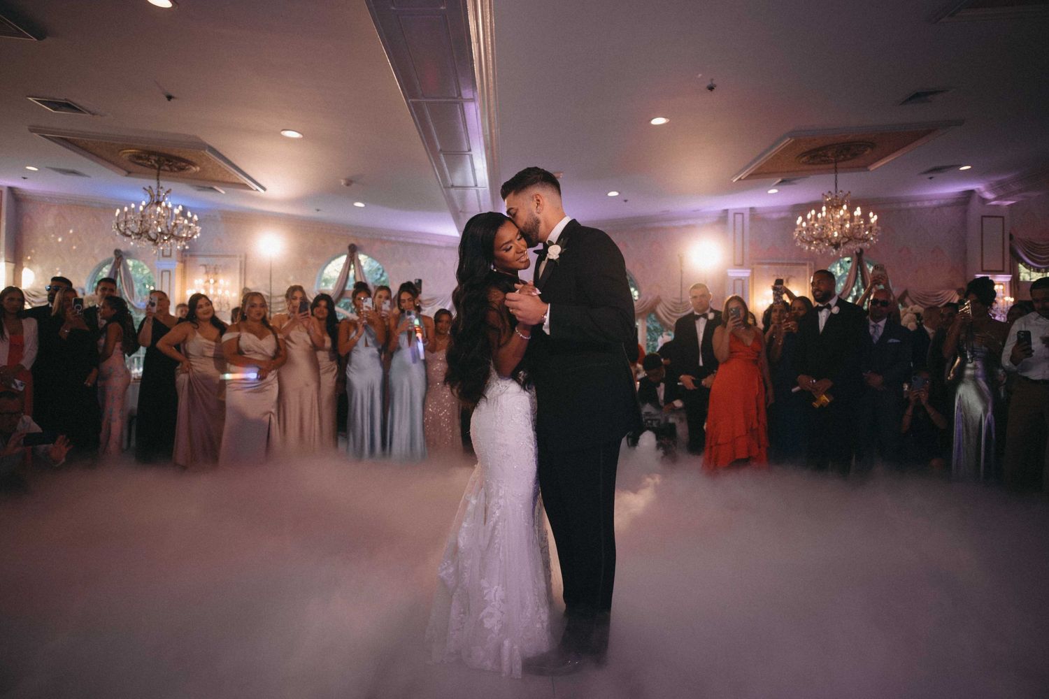 Bride and groom share first dance surrounded by low fog and wedding guests.