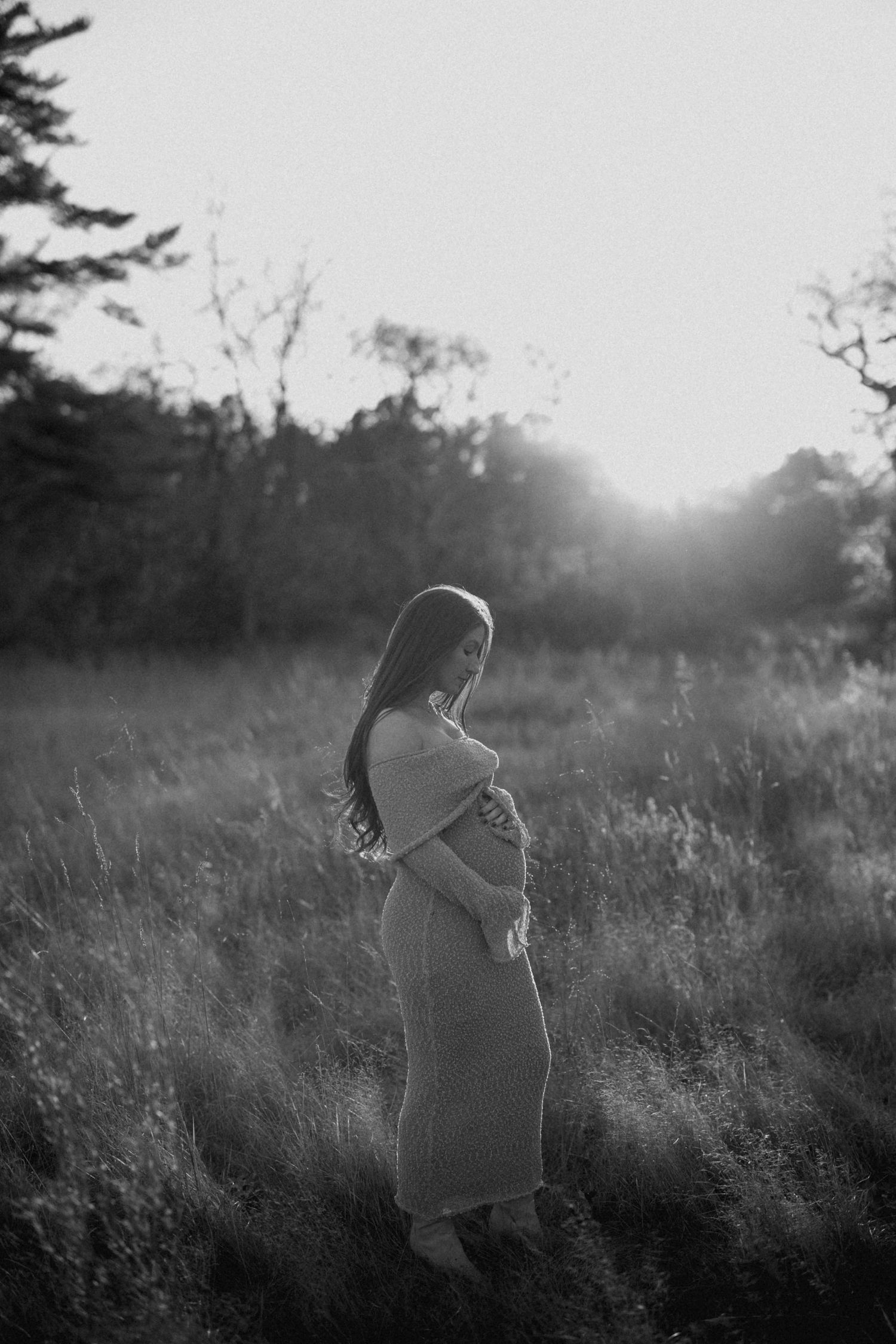Black and white portrait of pregnant woman in field during golden sunset.