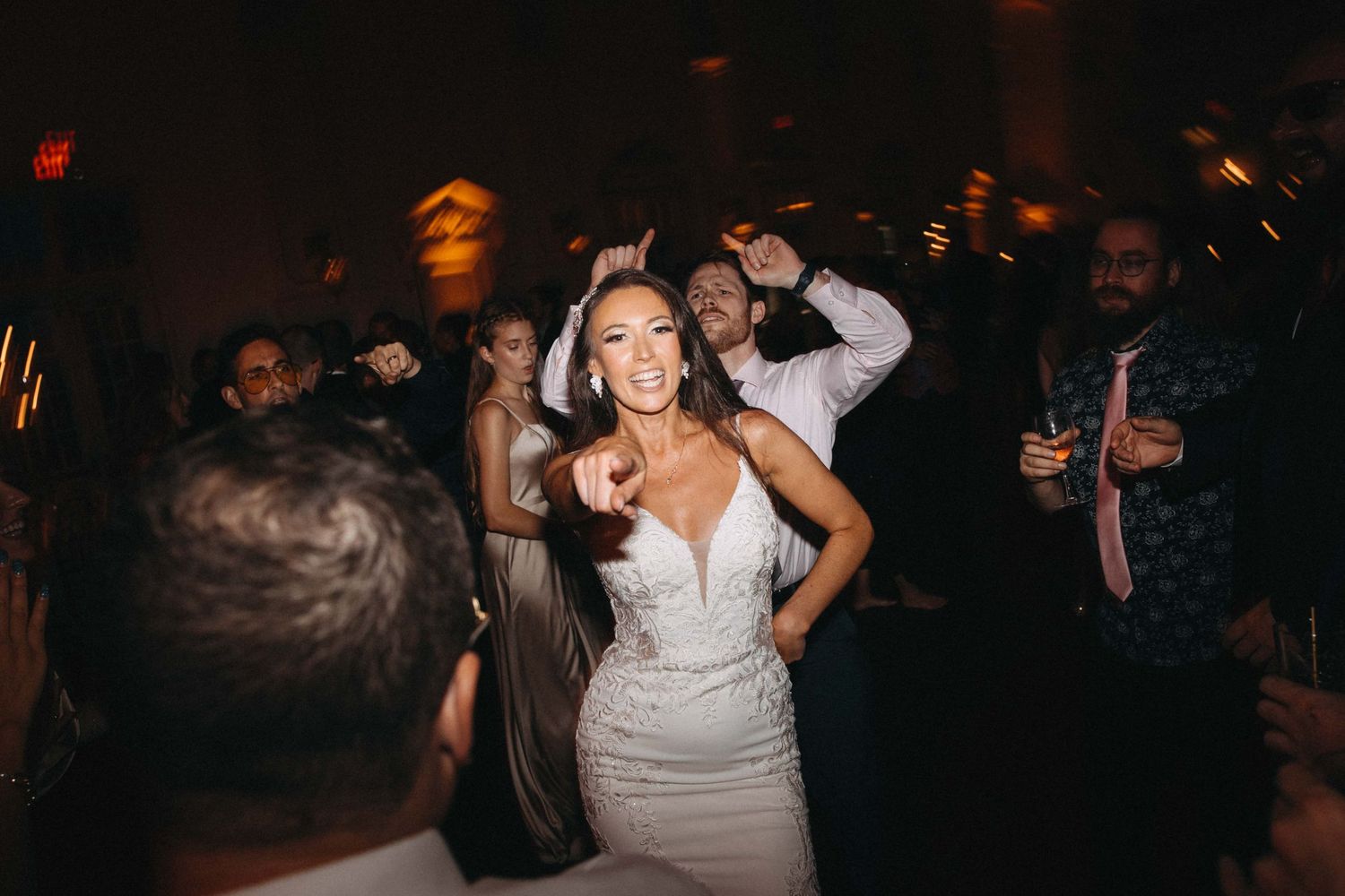 Radiant bride in fitted white gown dancing joyfully with guests during lively wedding reception celebration.