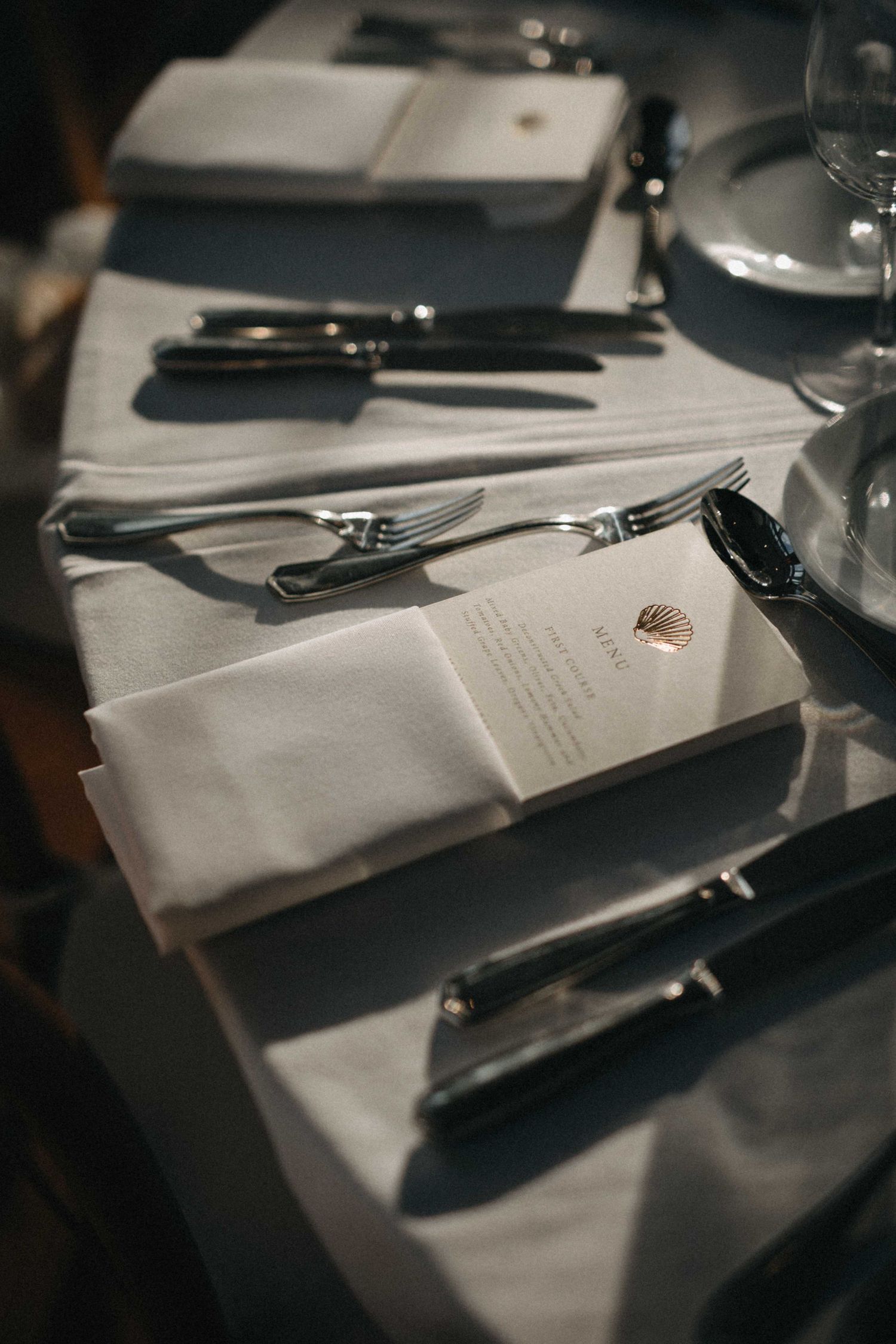 Elegant wedding reception place settings with white linen napkins, silverware, and printed menu cards on tables.