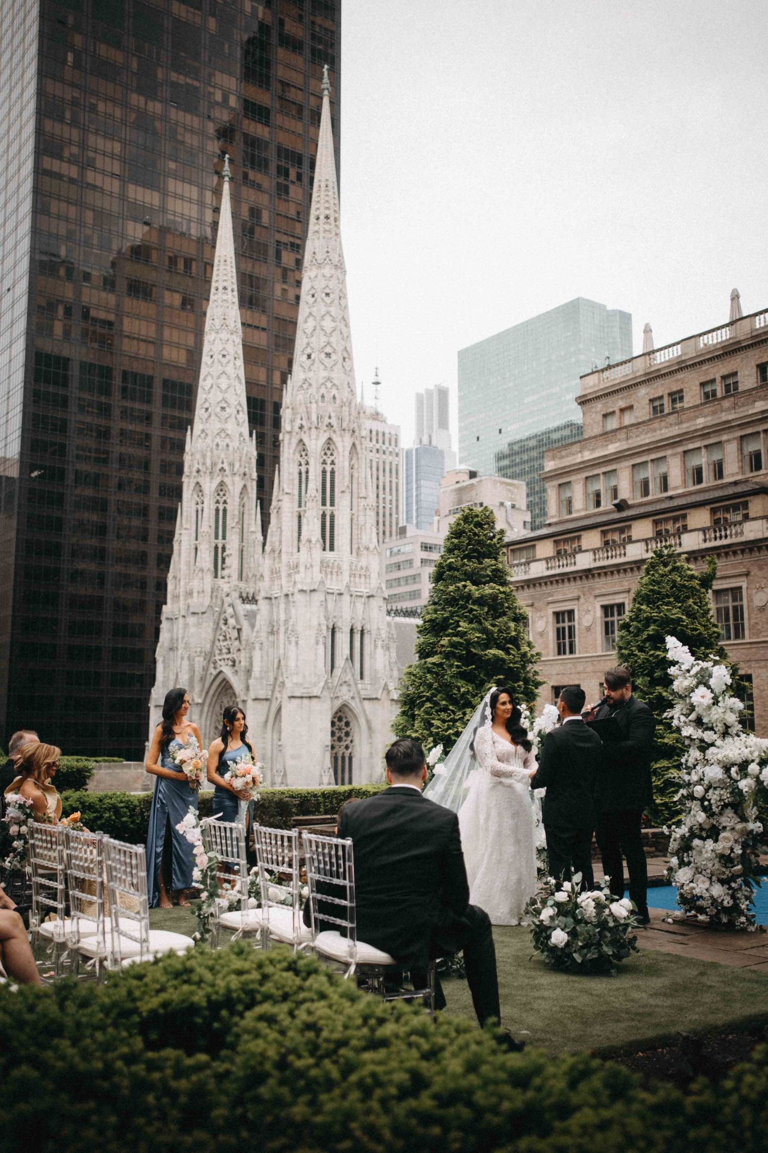 Rooftop wedding ceremony with St. Patrick's Cathedral backdrop in NYC, bride in white gown with veil.
