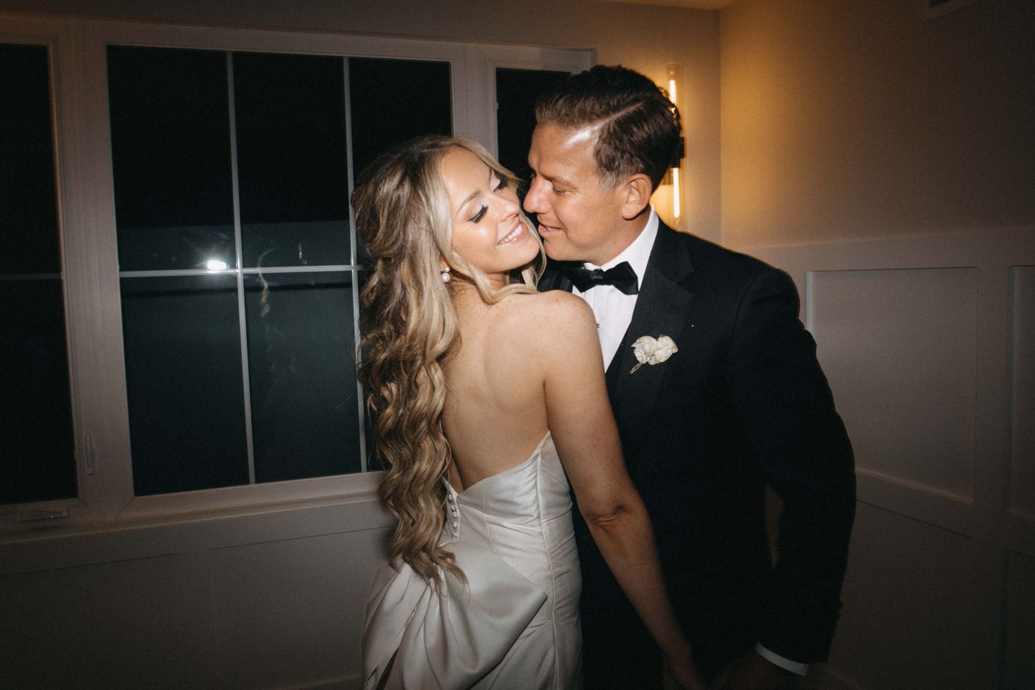 Smiling bride in strapless gown and groom in tuxedo share a joyful moment at their reception.