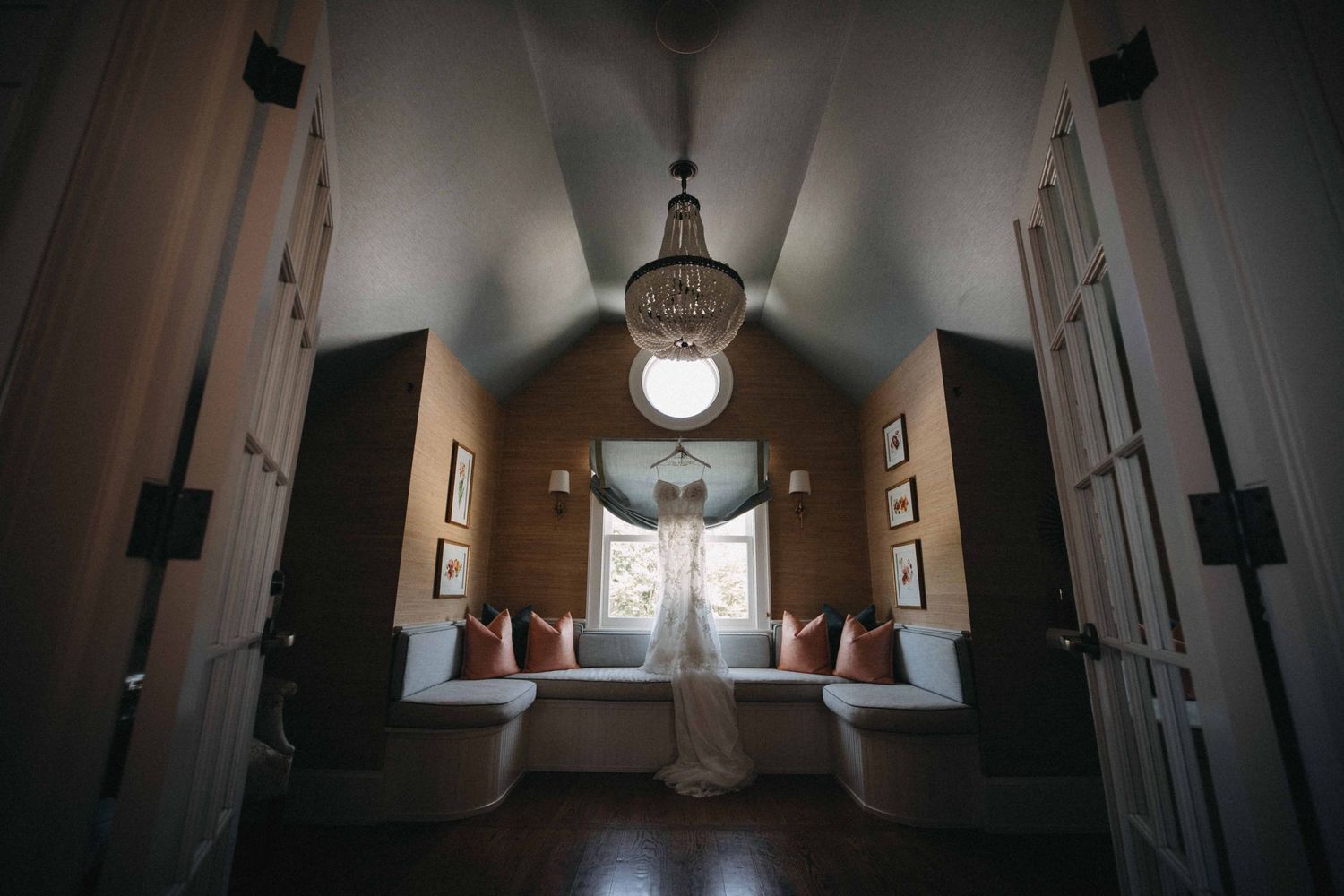 Wedding dress displayed in charming vaulted bridal suite with chandelier and window seat.