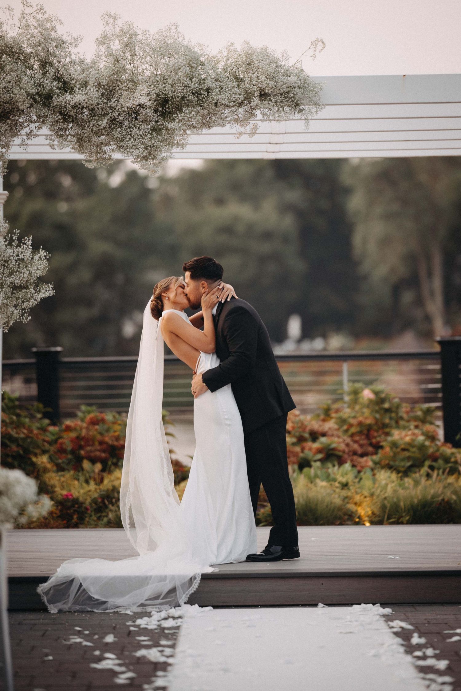 Bride and groom share their first kiss under a floral arch at an outdoor garden ceremony.