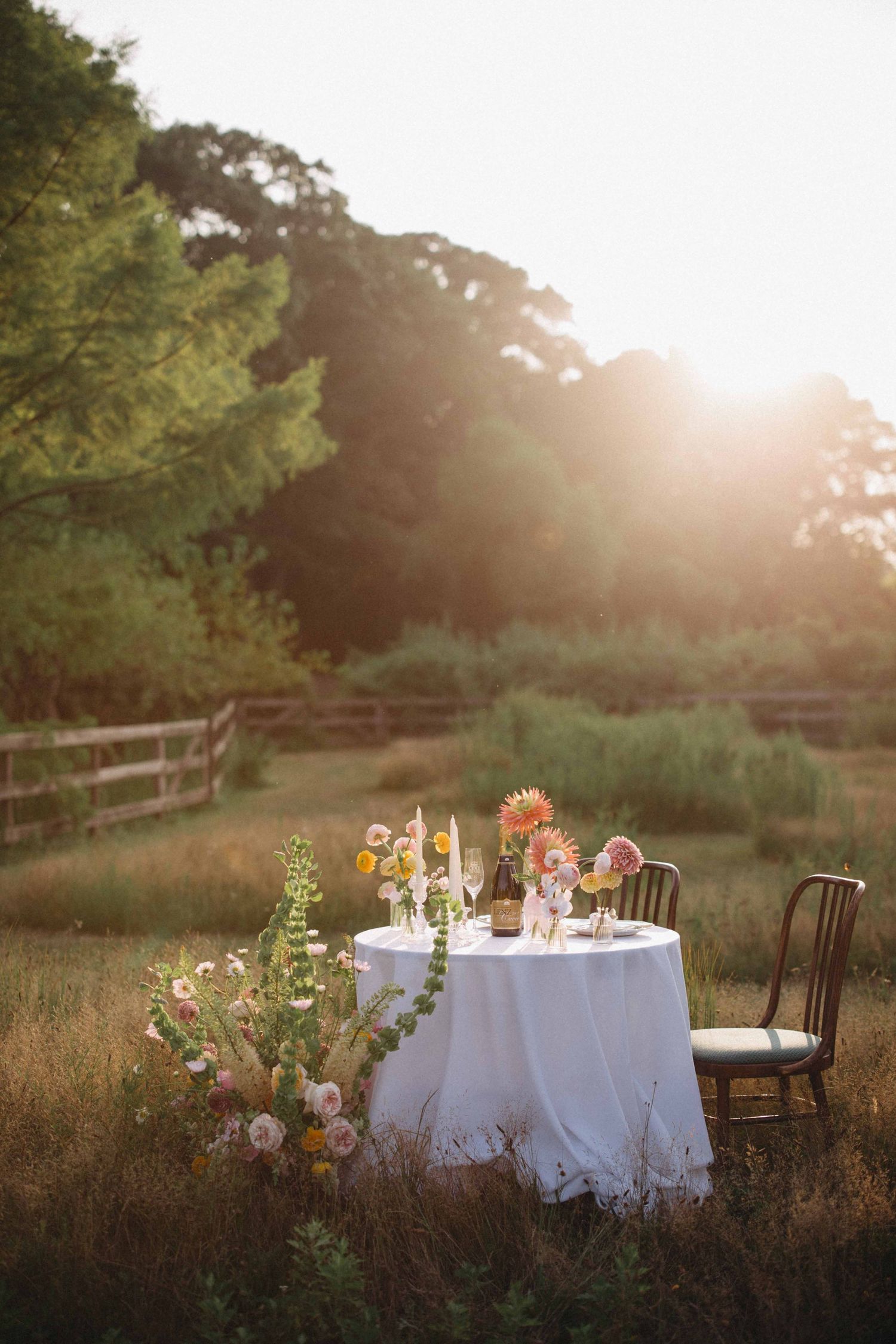 Elegant outdoor table with white linen and colorful floral arrangements glowing in golden sunset light.