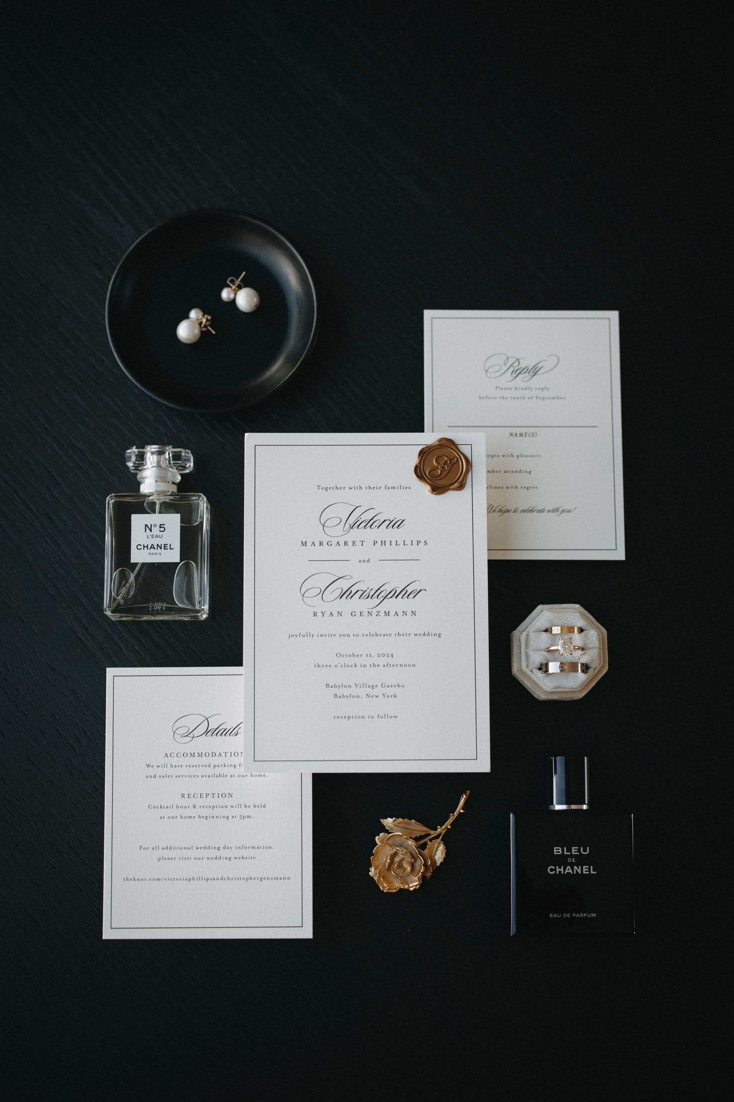 Elegant wedding invitation suite with Chanel perfume, pearl earrings, gold wax seal, and rings on dark background.