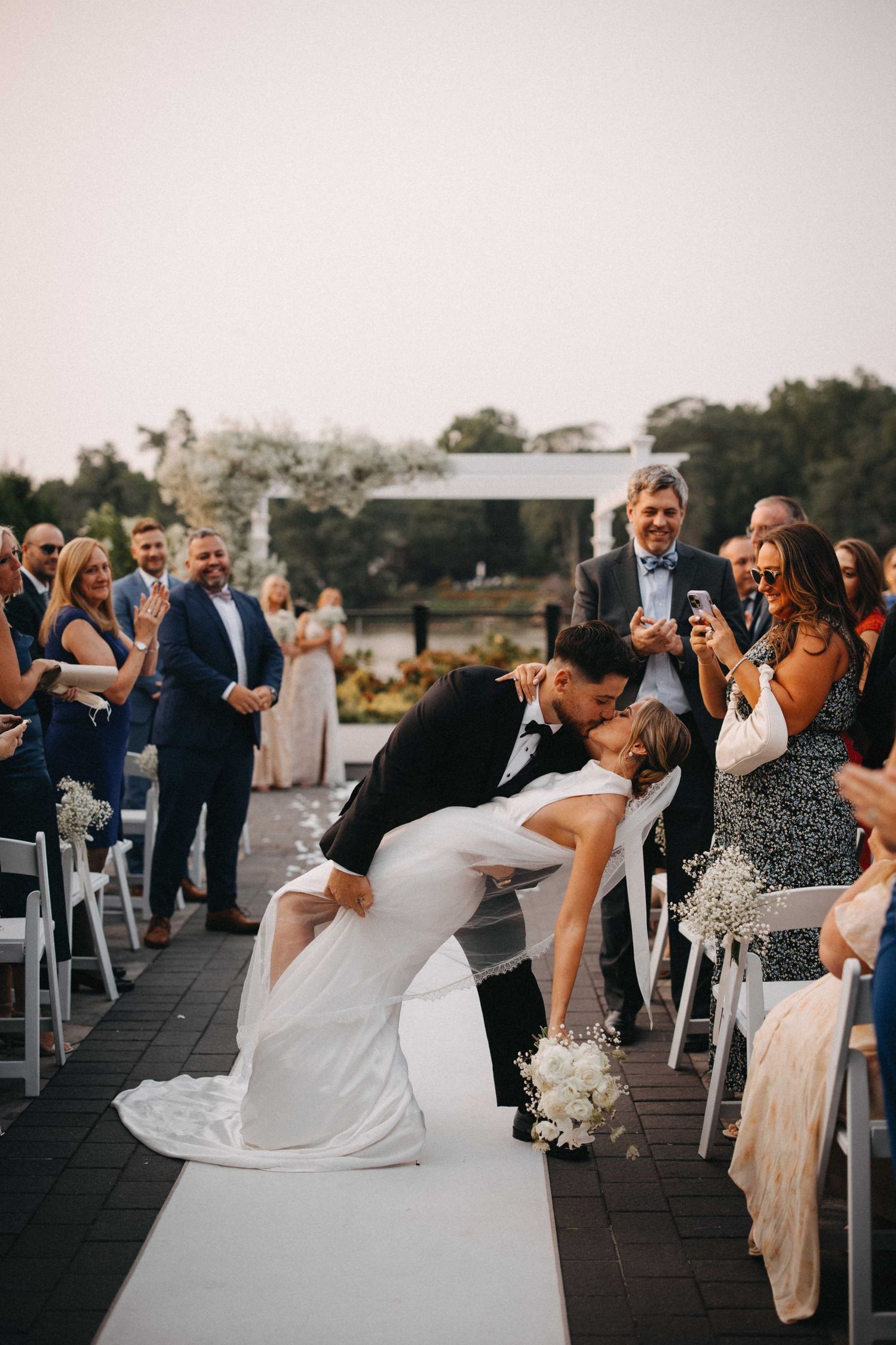 Groom dips bride for a romantic kiss while walking down the wedding aisle.
