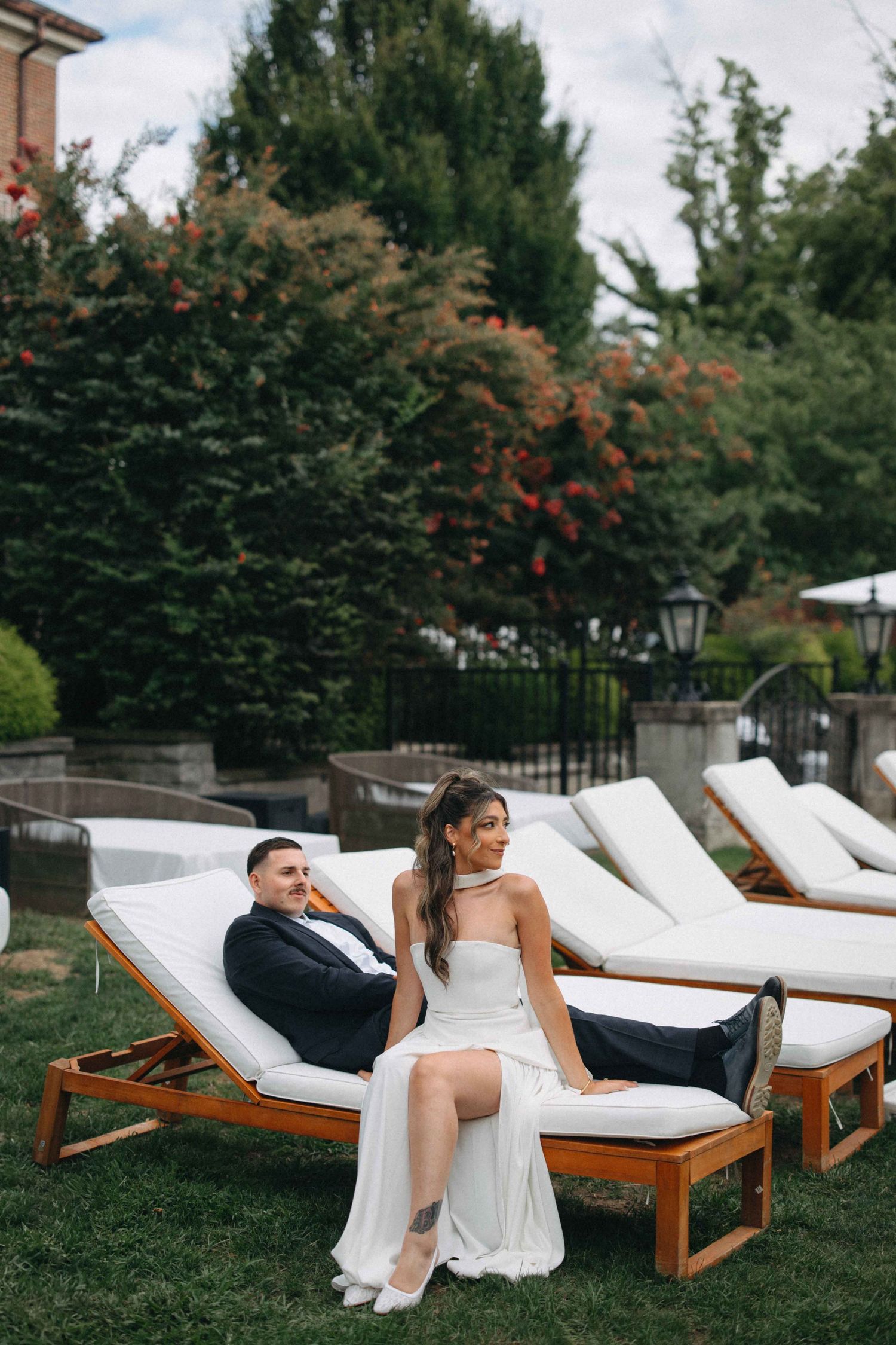 Bride and groom relaxing on wooden lounge chairs in a lush garden setting.