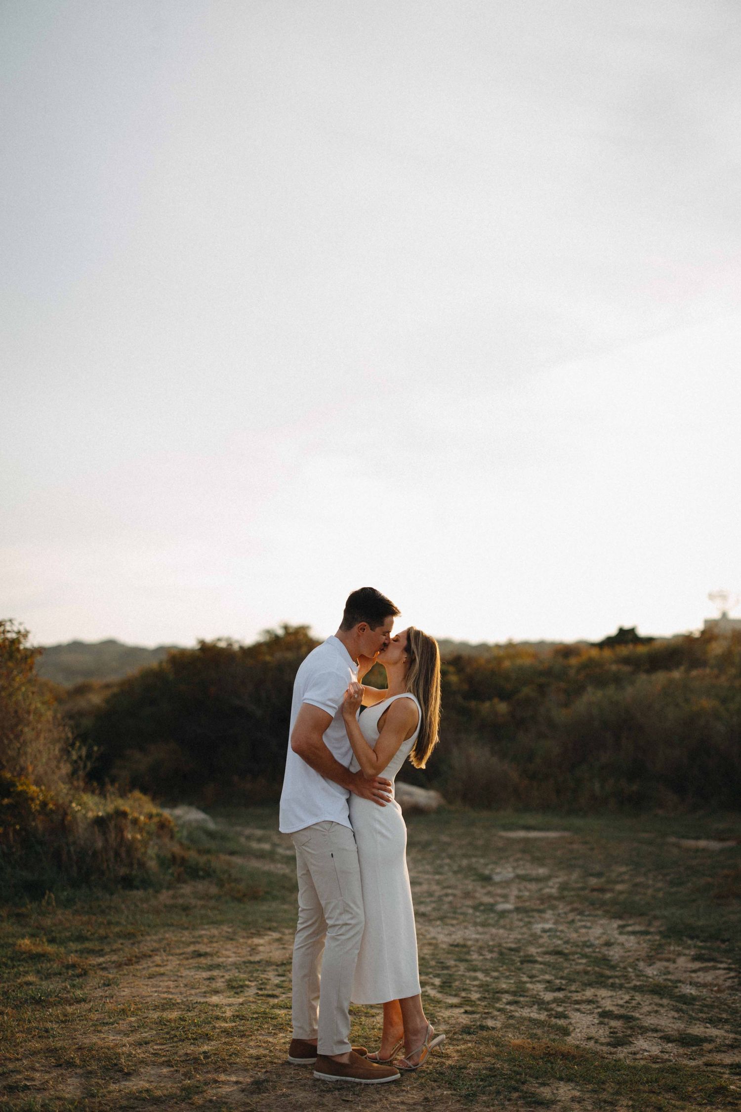 Couple sharing a romantic kiss in an open field at golden hour sunset.