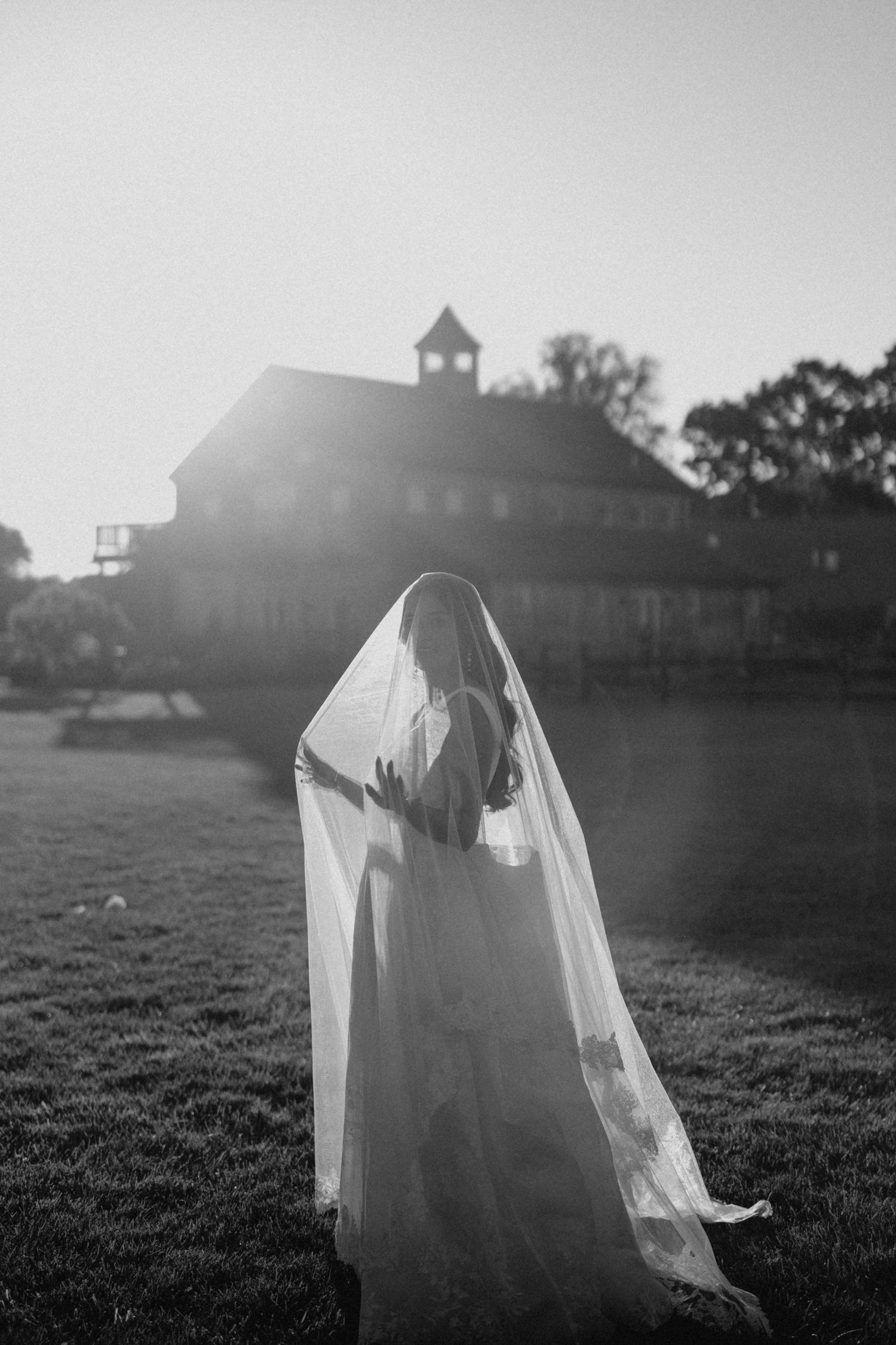 Black and white photo of bride in flowing veil and gown at sunset.