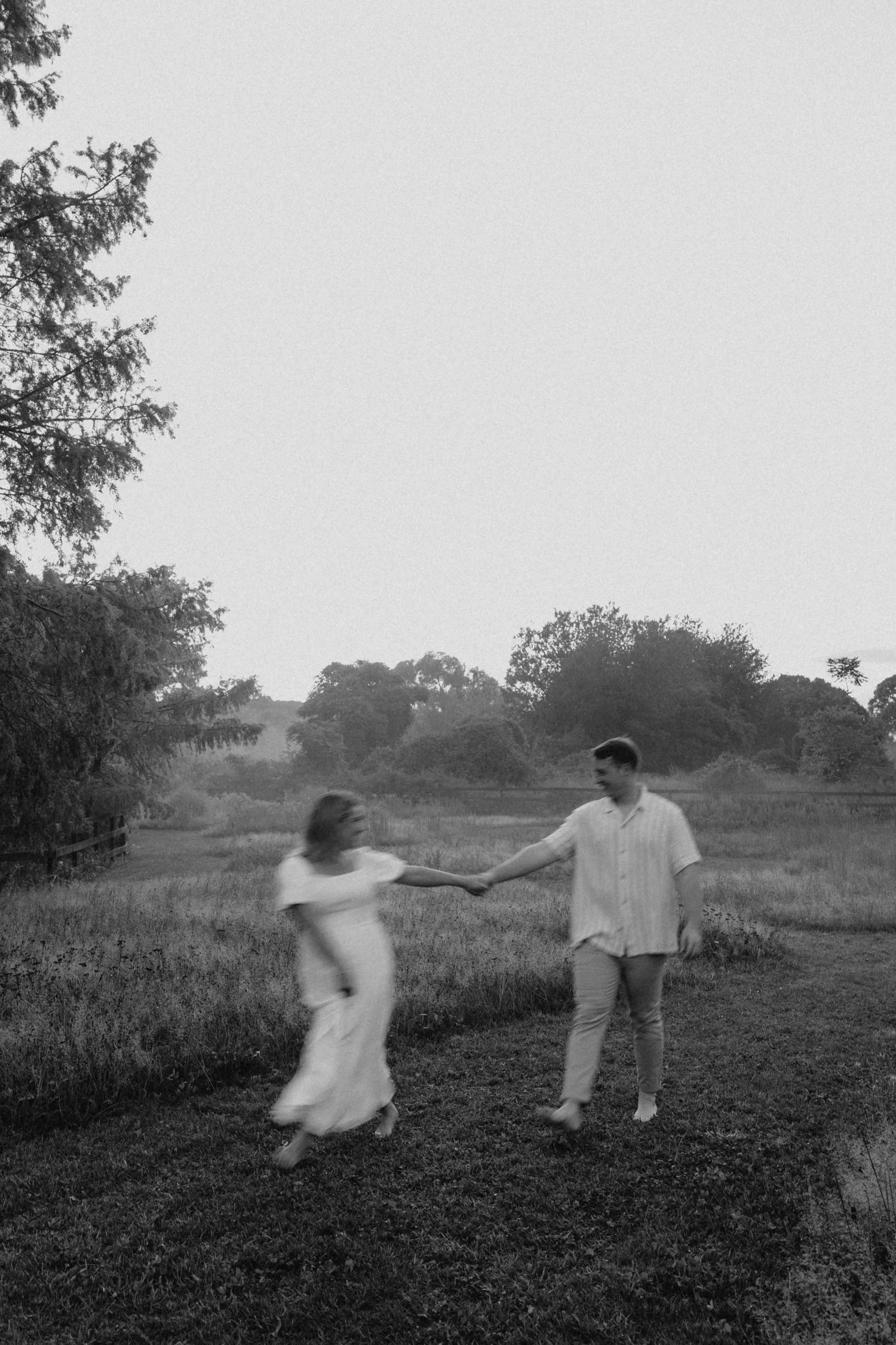 Black and white photo of a couple holding hands and walking along a rural path at dusk.