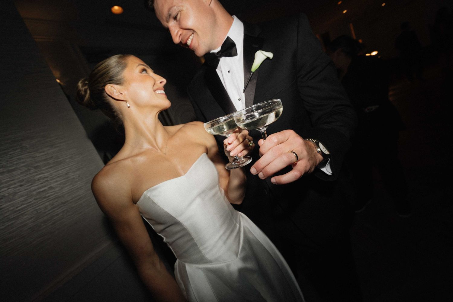 Bride and groom toasting with martini glasses at their wedding reception, smiling joyfully in formal attire.