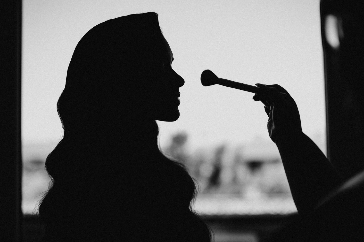 Black and white silhouette of a bride having makeup applied before her wedding ceremony.