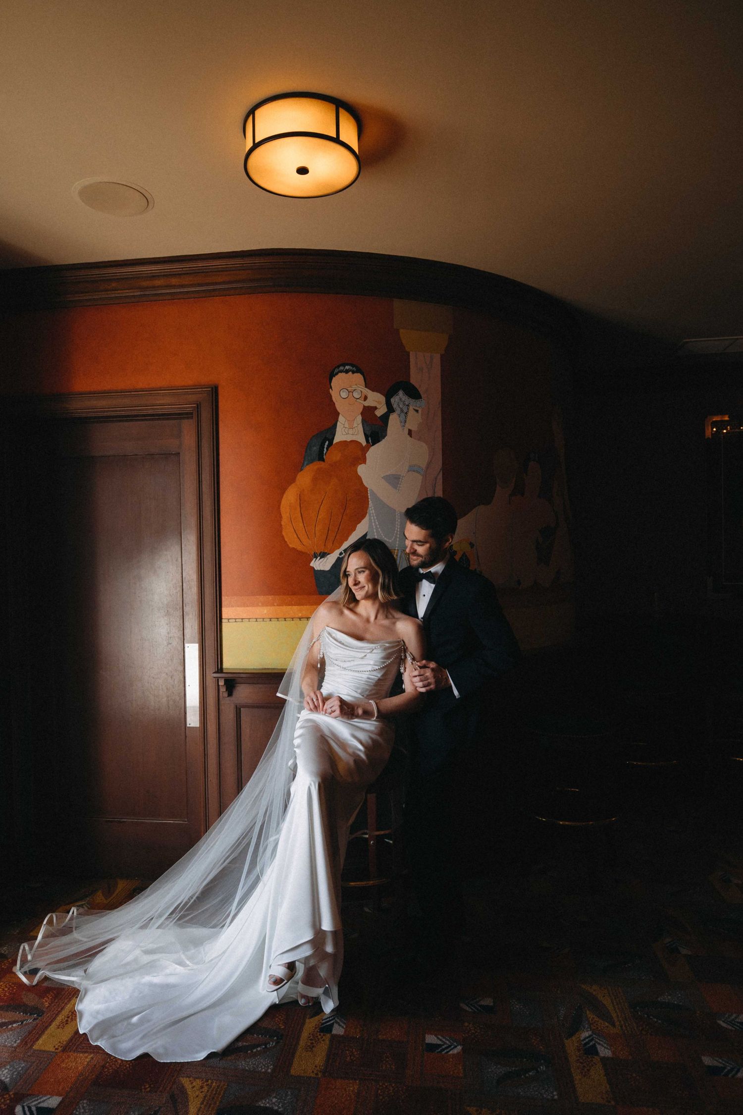 Bride and groom posing in warmly lit elegant venue with art deco decor.