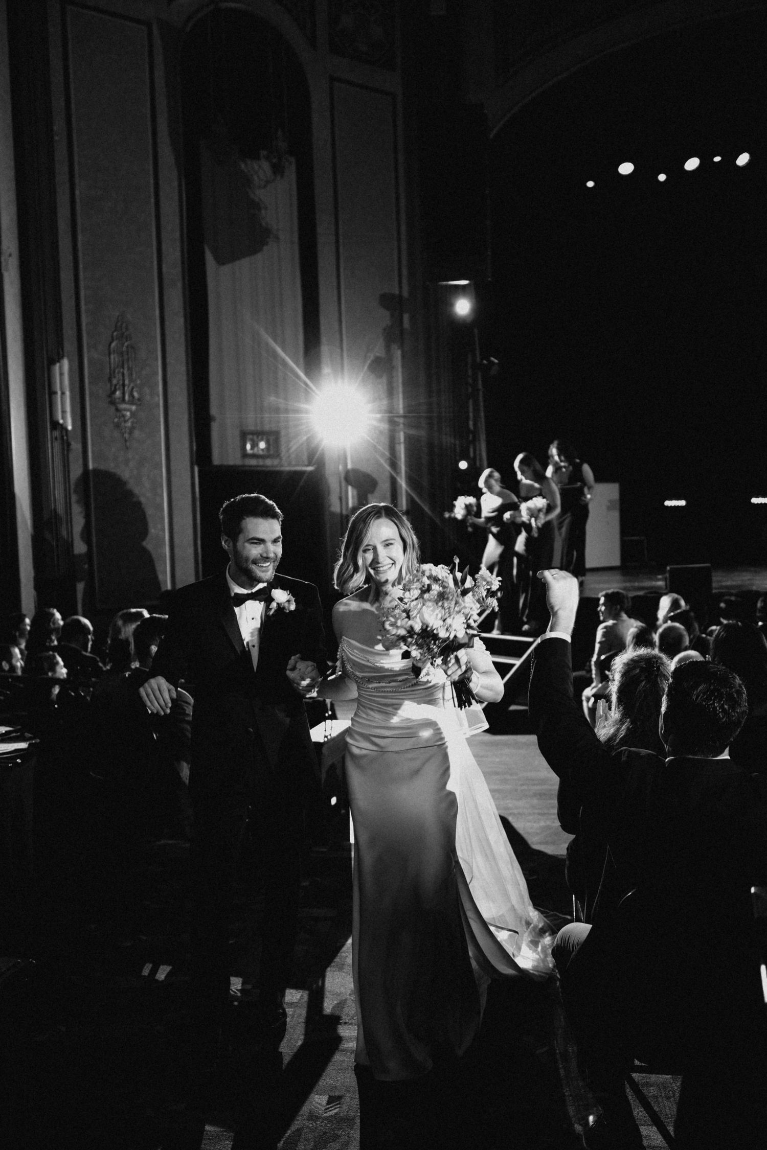 Joyful bride and groom walk back down the aisle after their wedding ceremony in a grand theater.
