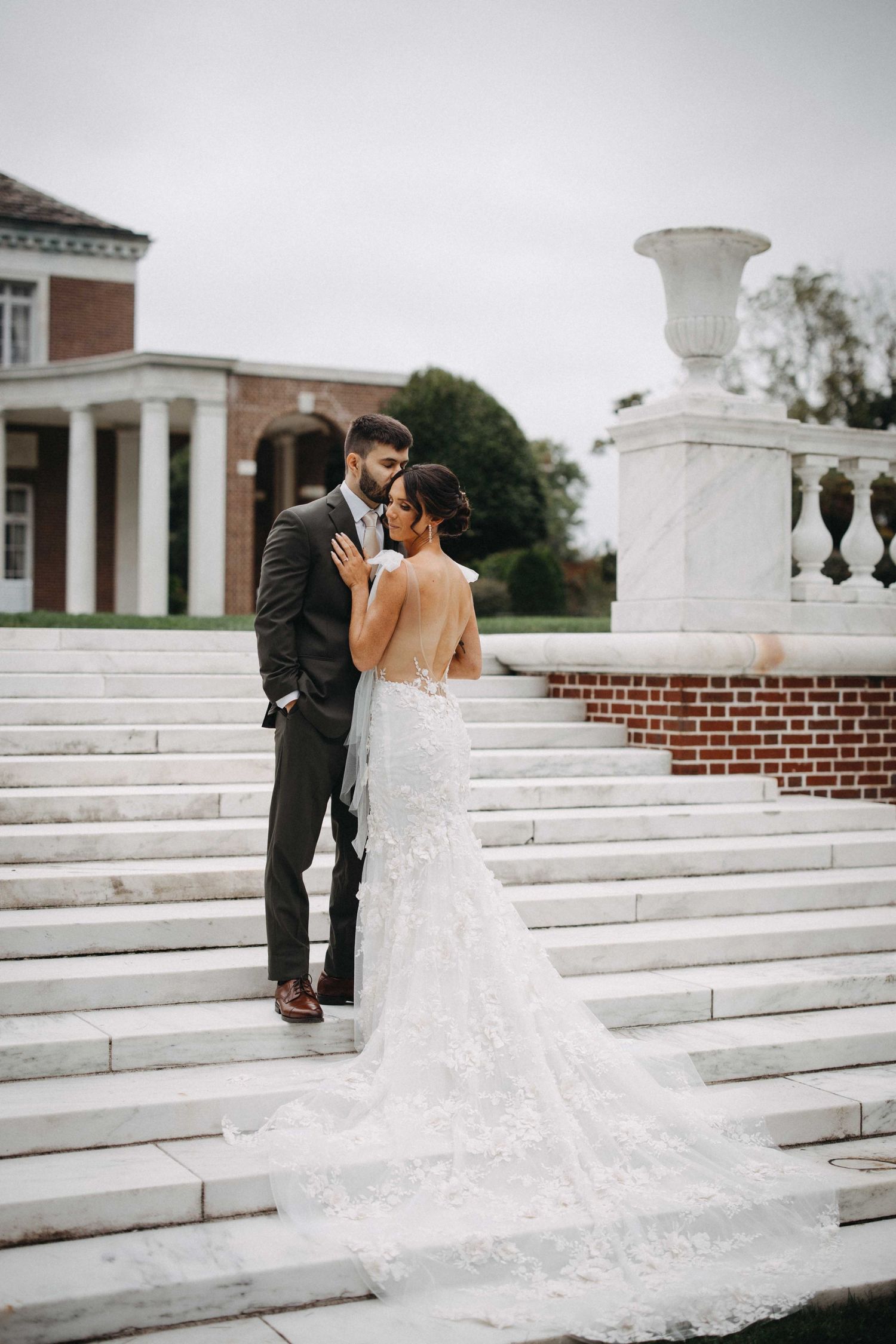 Bride and groom embracing on white marble steps outside a classic brick and marble wedding venue.