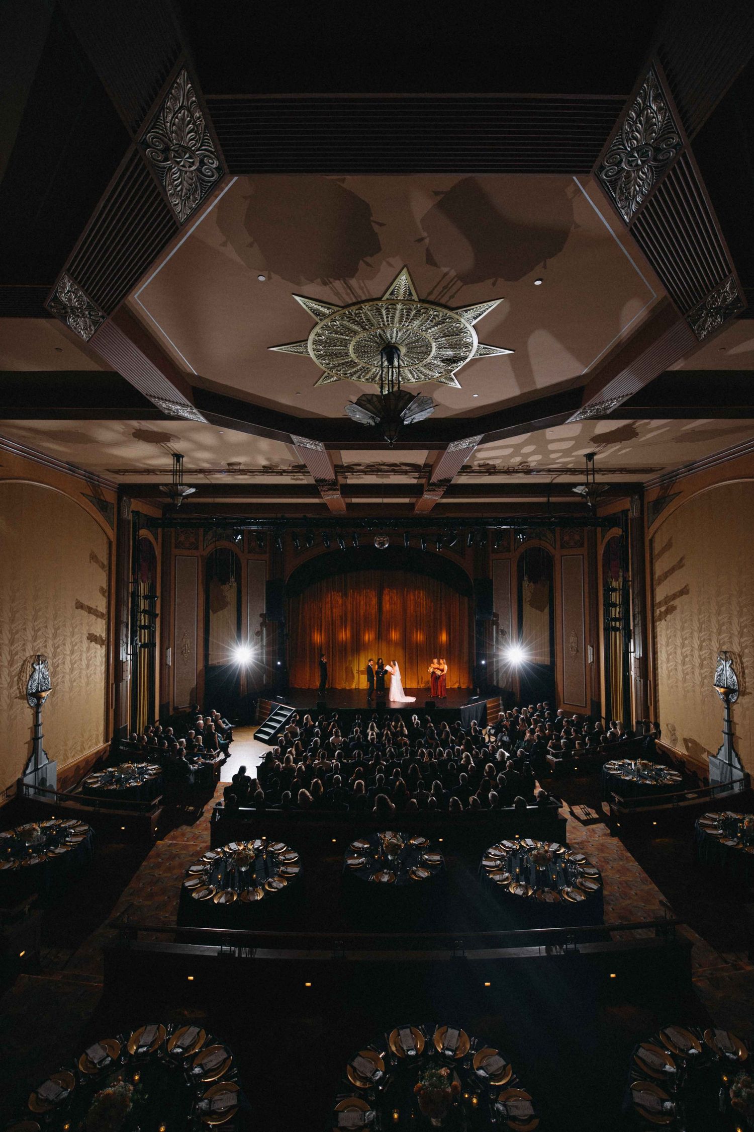 Aerial view of elegant wedding ceremony inside ornate Art Deco ballroom with star chandelier.