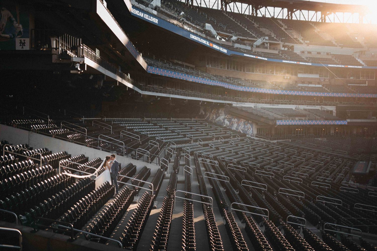 Empty stadium seats bathed in golden sunlight streaming through the upper deck of a large sports arena.