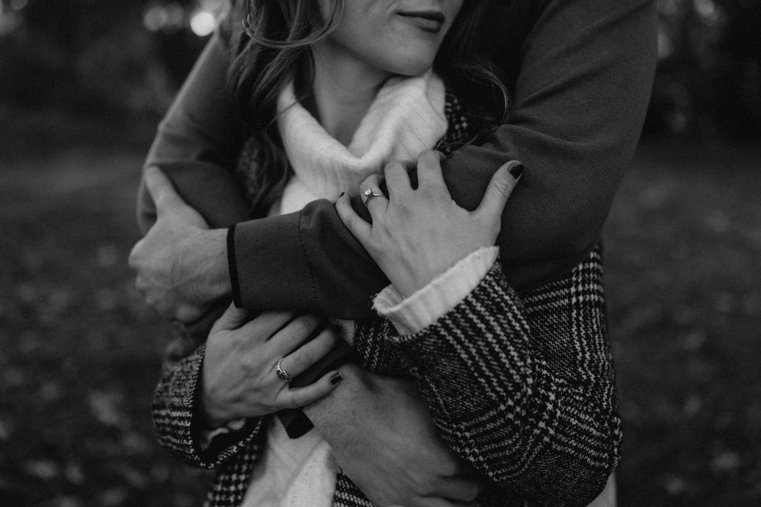 Black and white close-up of a man wrapping his arms around a woman in a plaid coat.