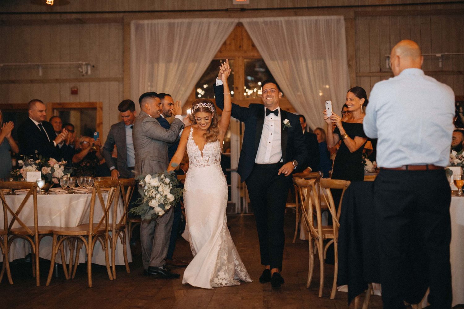 Bride and groom make grand entrance into rustic barn reception as guests celebrate.