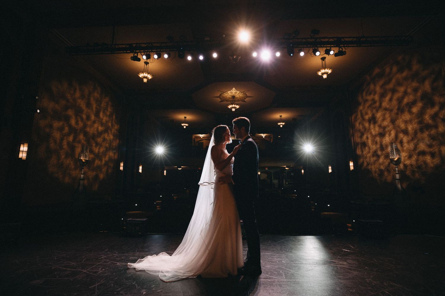 Bride and groom share a romantic silhouette moment on the dance floor of a warmly lit wedding venue.