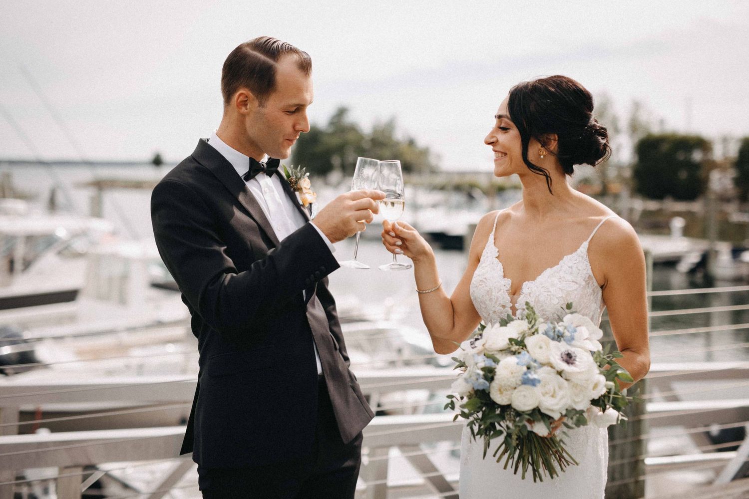 Bride and groom toasting champagne glasses at waterfront marina on their wedding day.