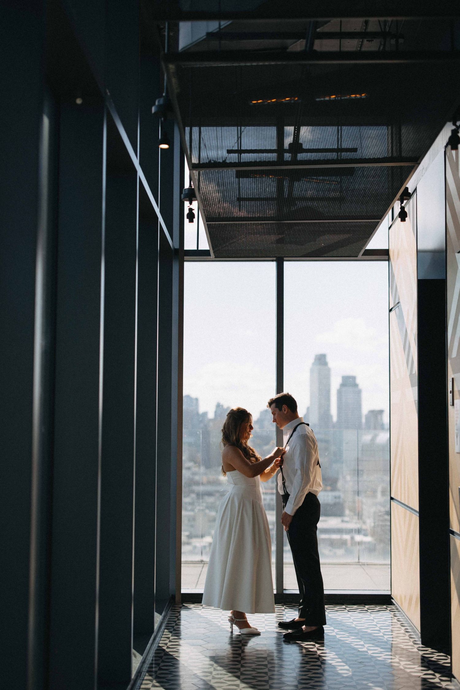 A bride and groom share a romantic moment in a modern corridor with city skyline views.