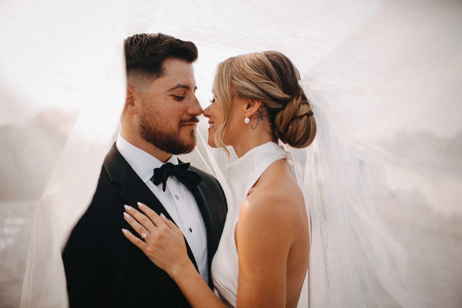 Bride and groom share an intimate moment under a flowing white veil on their wedding day.