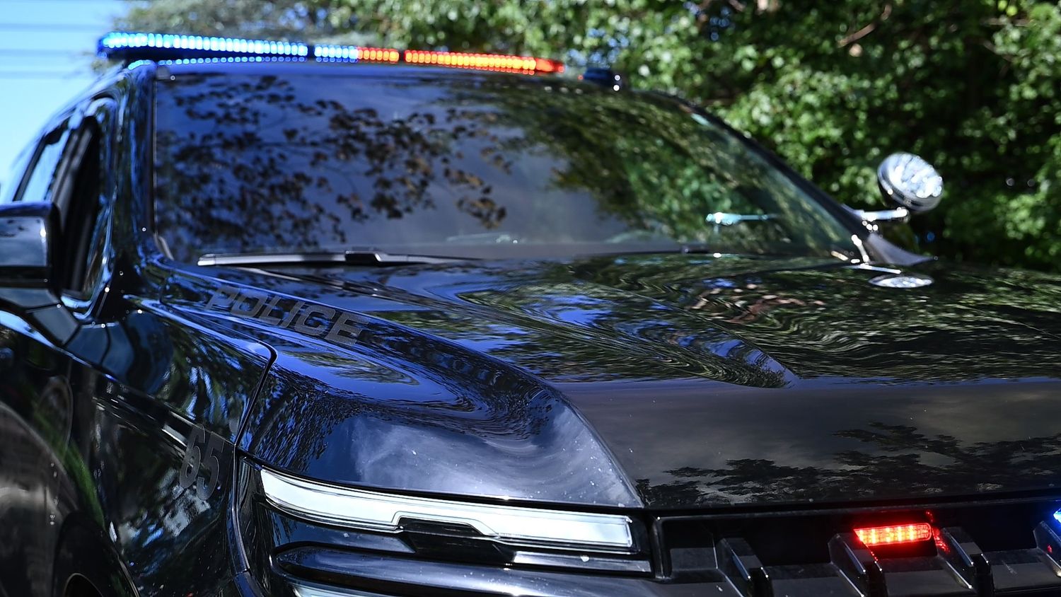 Black police SUV with blue and orange emergency lights on roof, parked near trees.