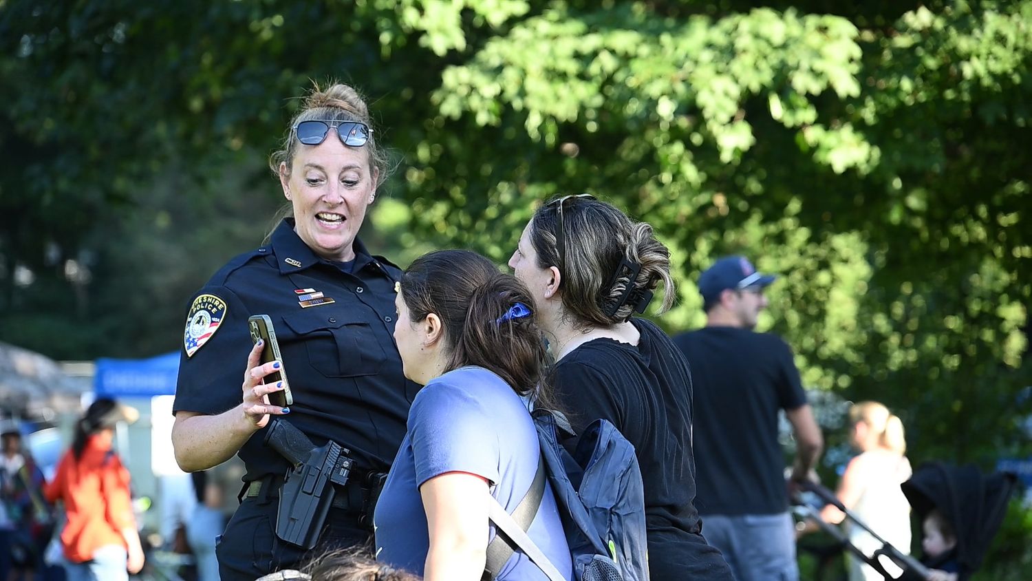 Female police officer smiling and interacting with civilians at an outdoor community event in a park.