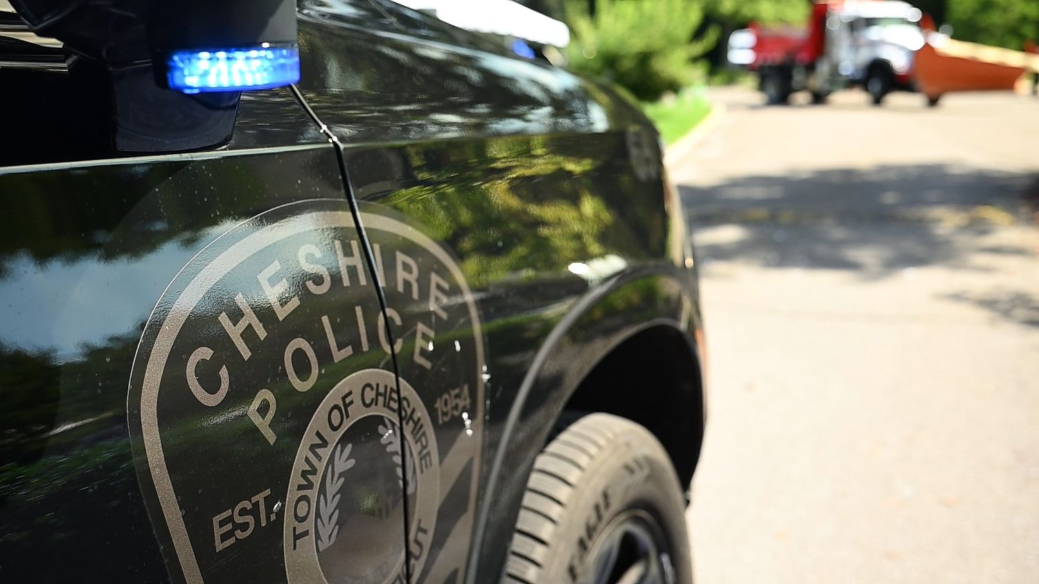 Close-up of a Cheshire Police Department patrol car door with badge emblem and blue emergency light.