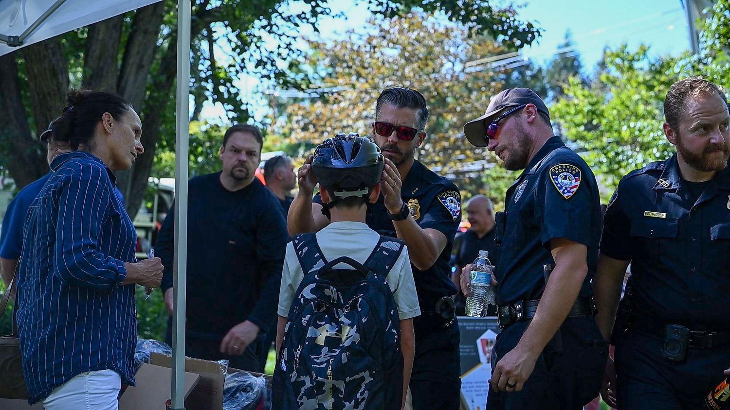 Police officers help a child try on a bicycle helmet at an outdoor community event on a sunny day.
