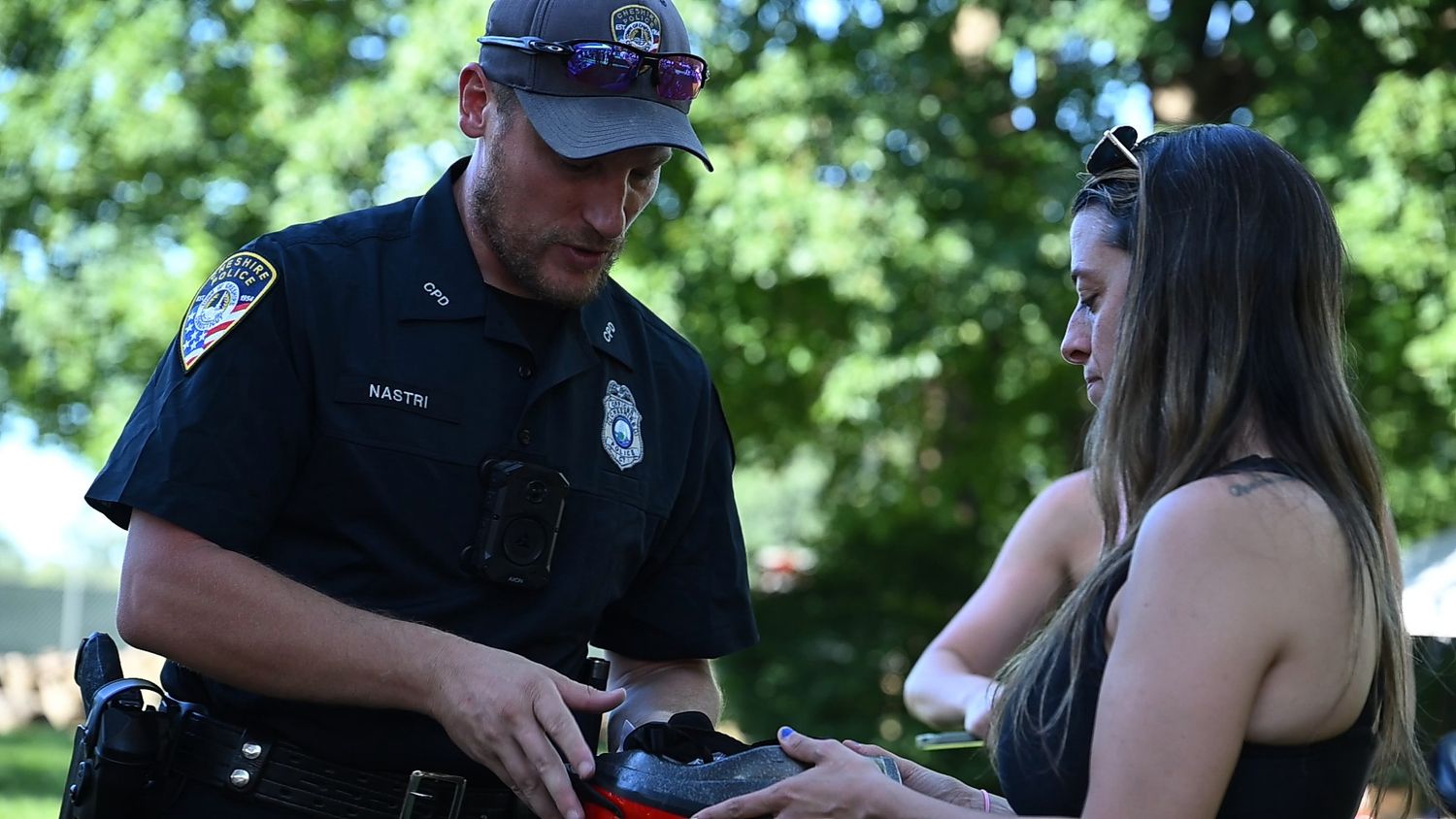 Police officer checking ID of a young woman outdoors in a park on a sunny day.