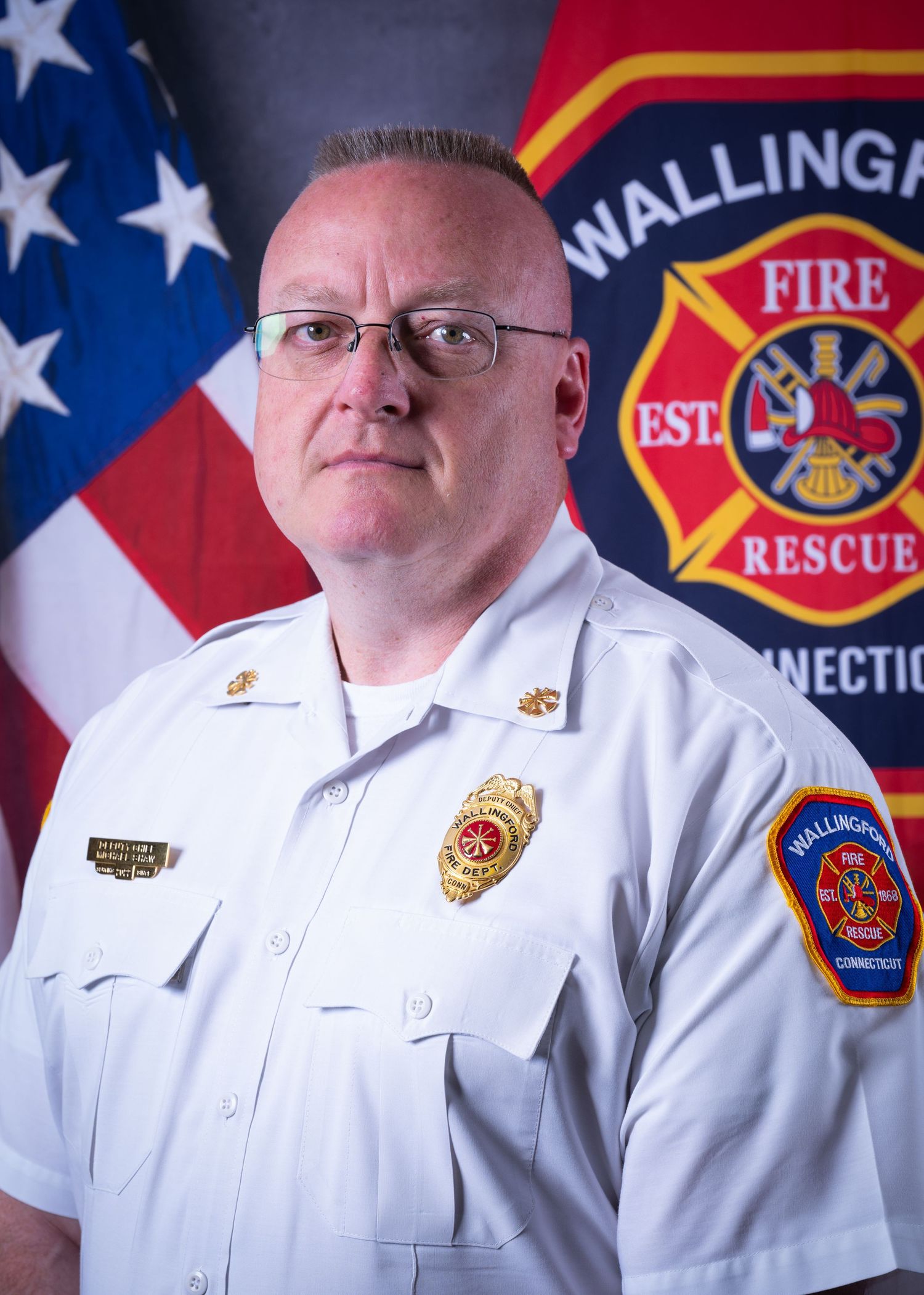 Wallingford Fire Rescue officer in white uniform shirt posing before an American flag and department logo.