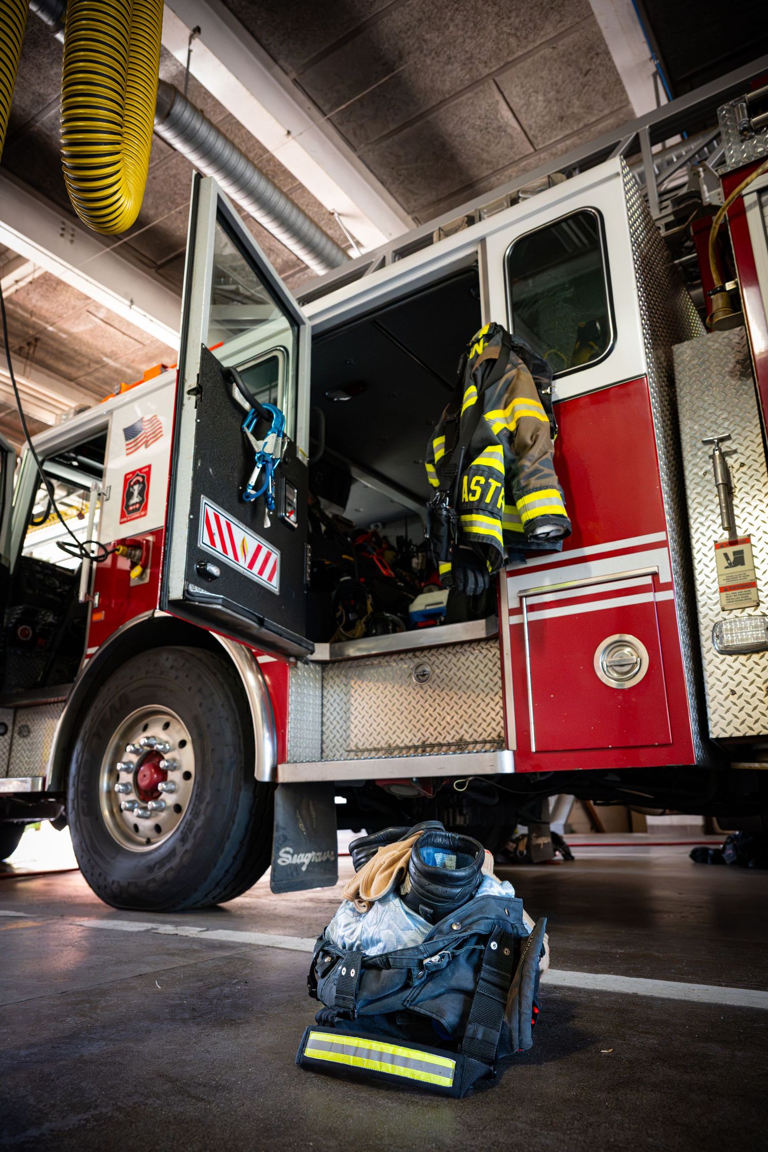 Red fire truck with open door showing turnout gear hanging inside and SCBA equipment on the station floor.