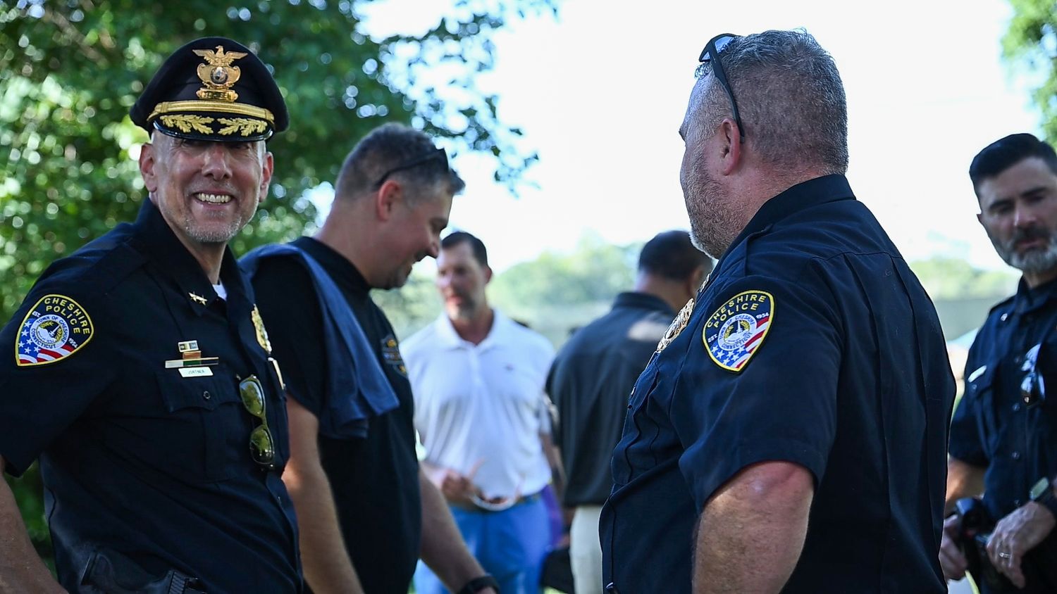 Police officers in uniform smile and chat together at an outdoor community gathering on a sunny day.
