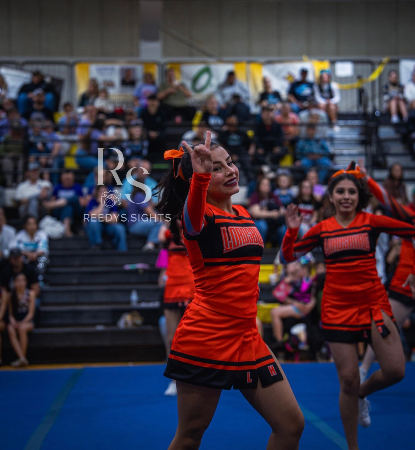 Cheerleaders in red uniforms perform synchronized dance moves during a high school sports event.